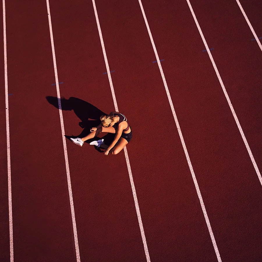 Runner sitting and resting on a red track lane, casting a shadow in the late afternoon sun