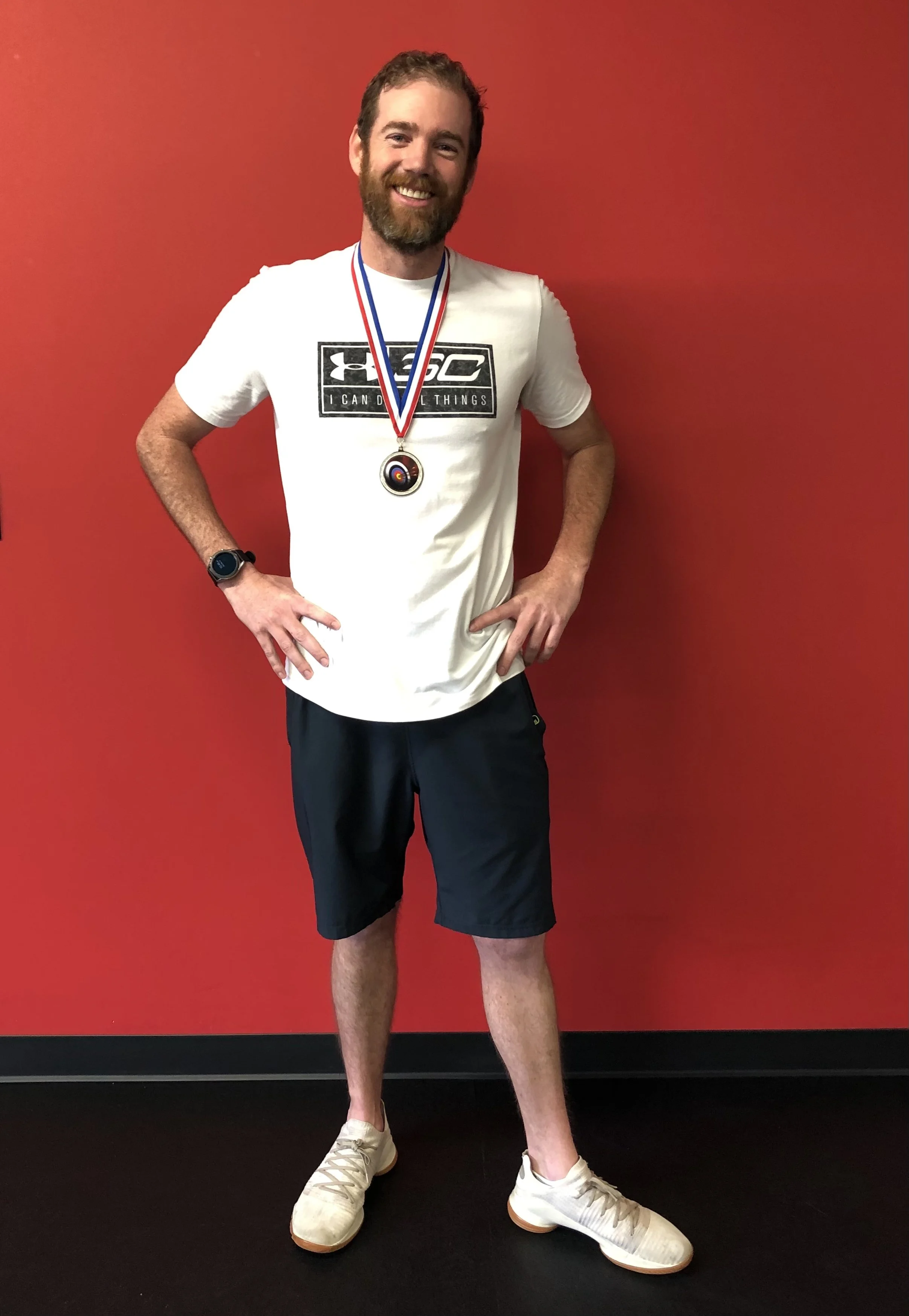 Athlete Instincts member wearing an award medal and standing in front of a red wall, with other awards and certificates visible in the background.