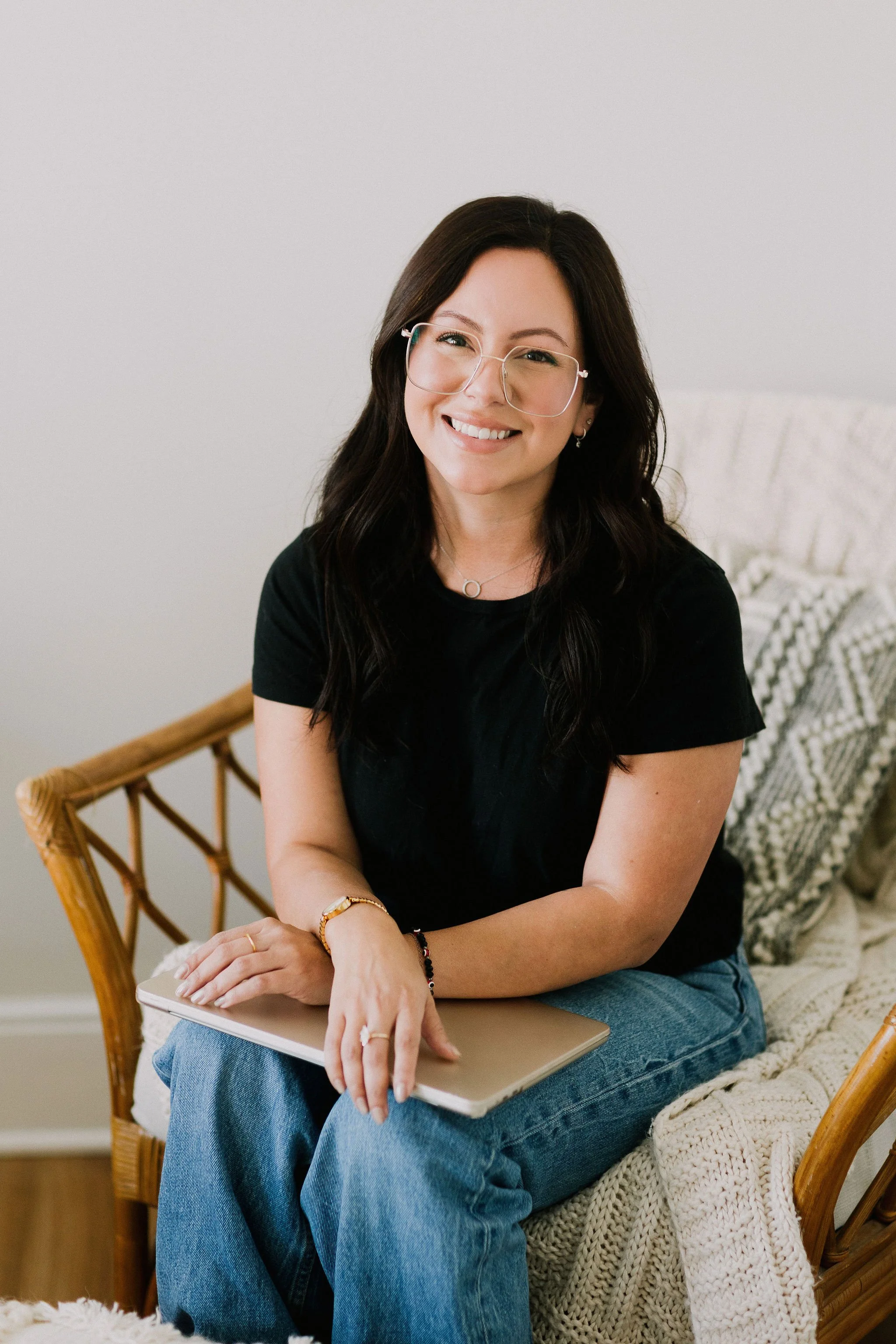 A kind supportive therapist sitting on a wicker chair with a laptop on her lap in a cozy room.