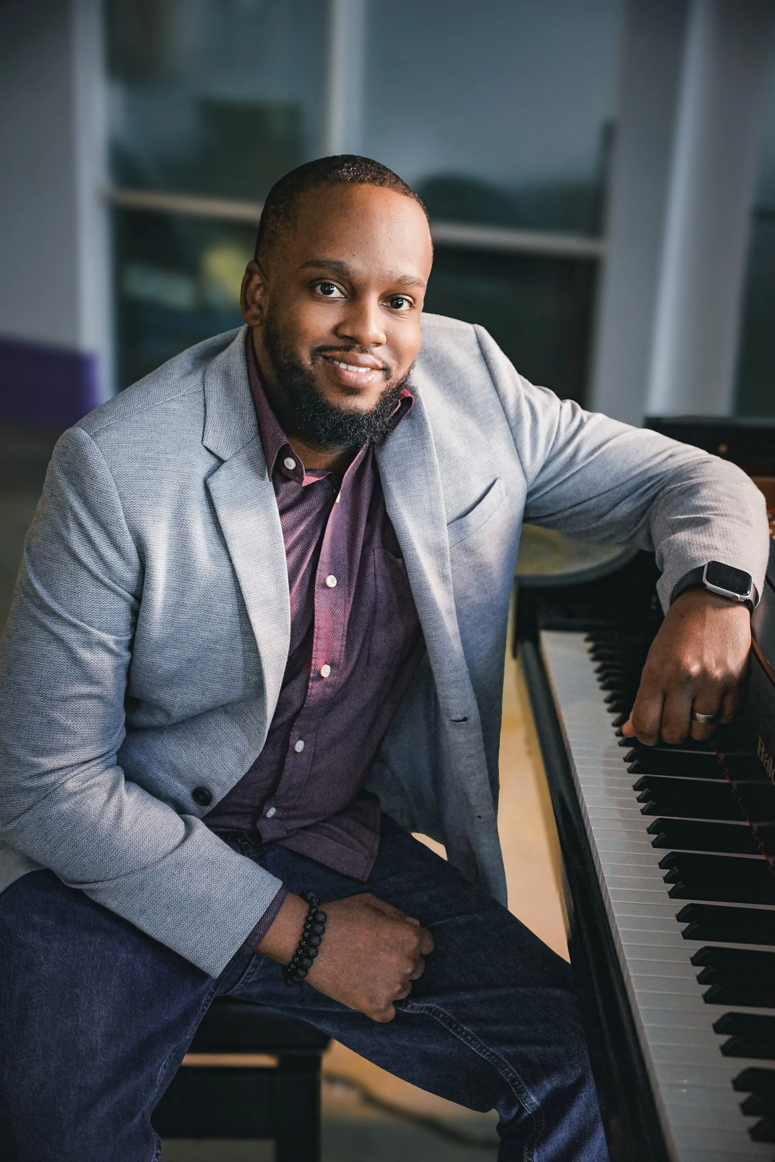 Myron sitting at a piano smiling, with his right arm resting on the piano.