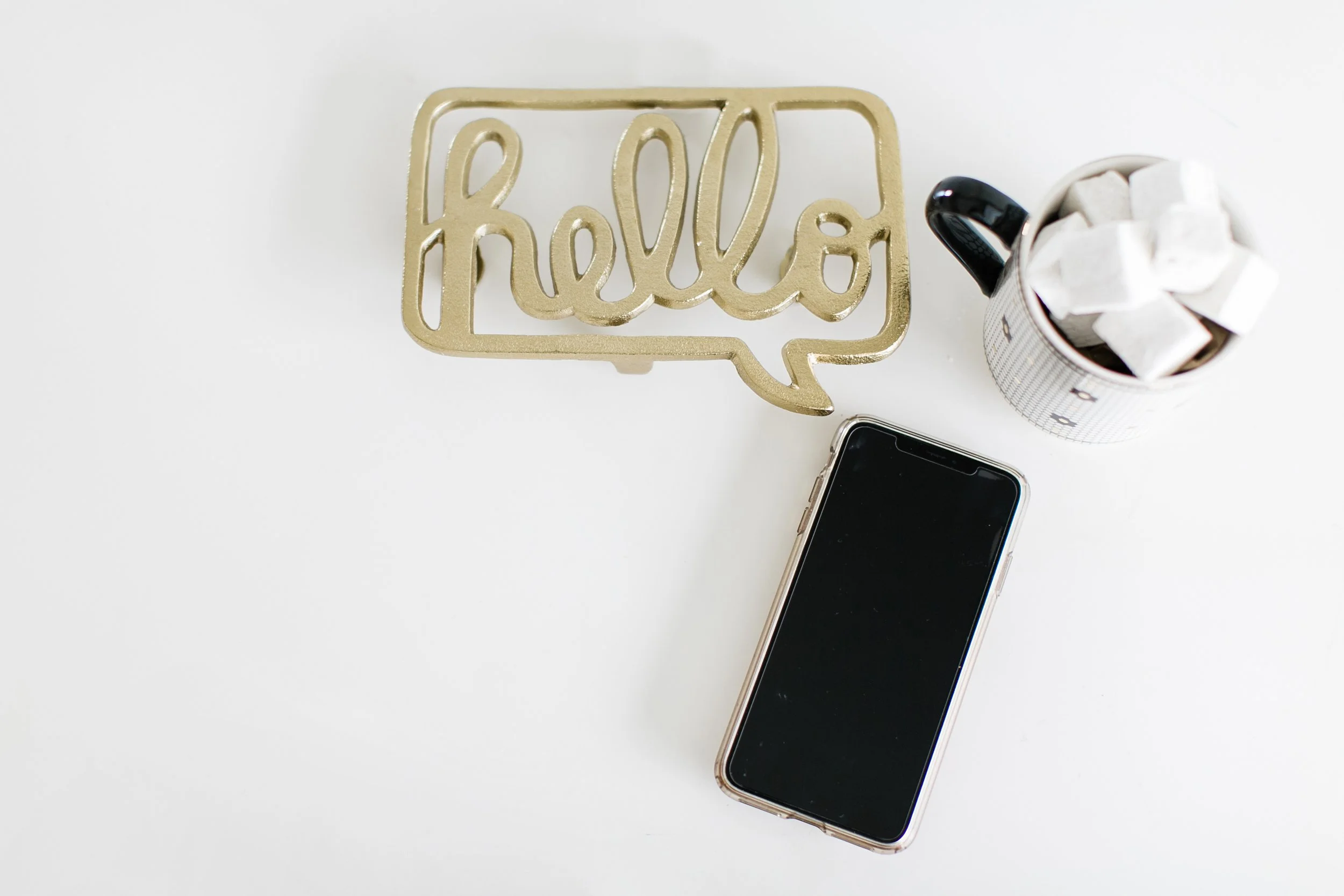 Gold word sculpture that says 'hello' next to a cup filled with sugar cubes, and a smartphone on a white surface.