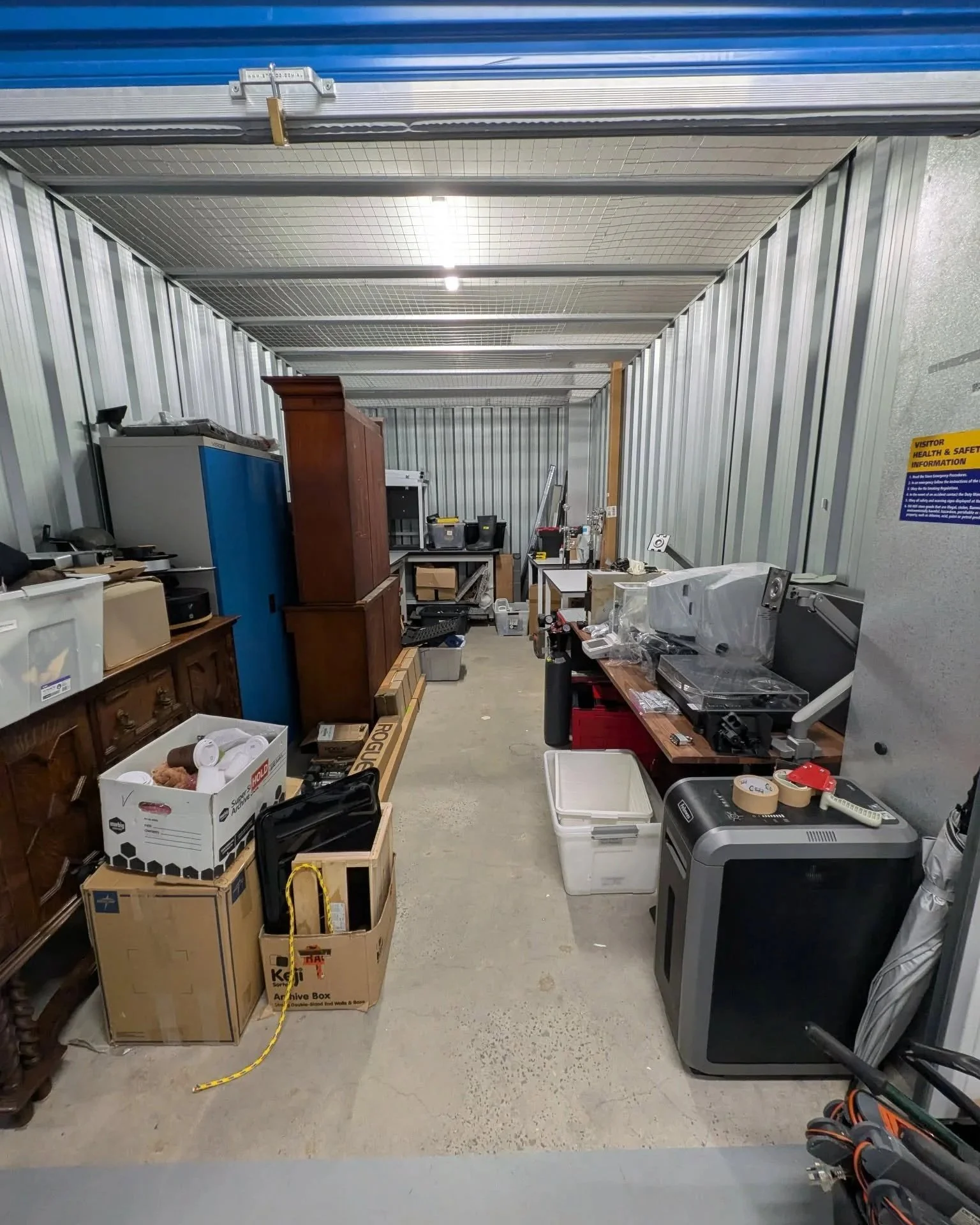Storage unit filled with various furniture, boxes, and tools.