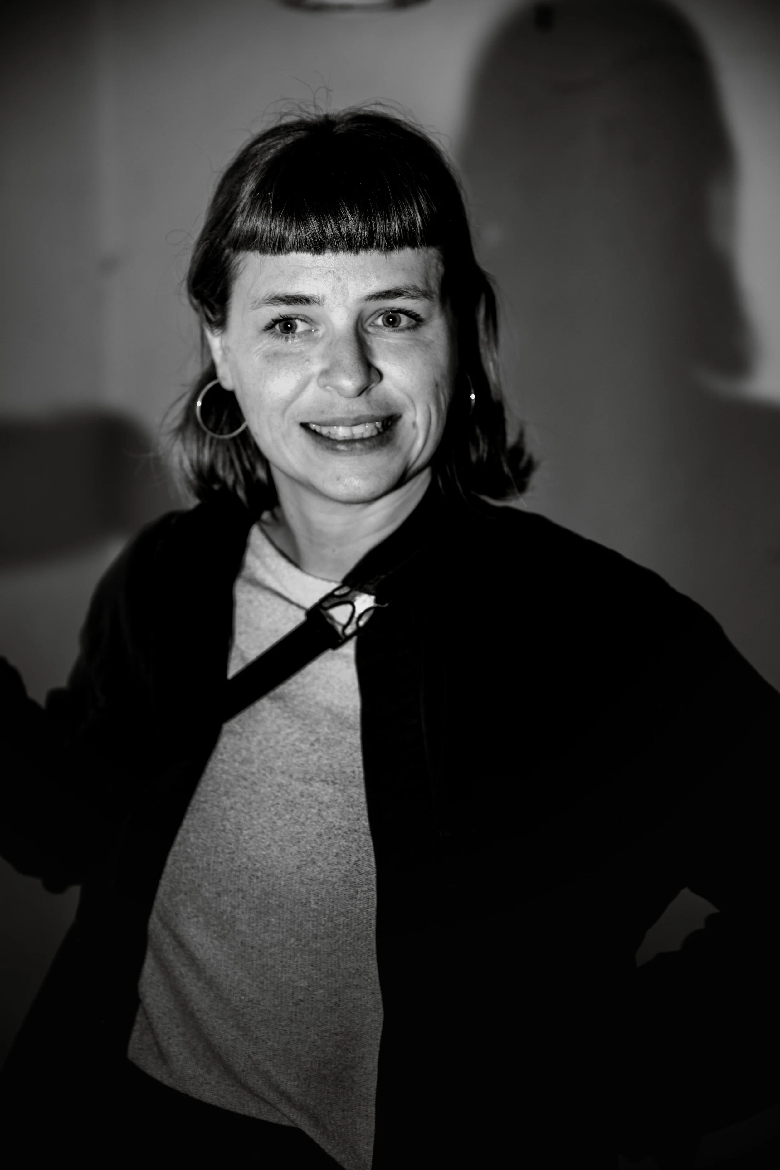 Schwarz-Weiß-Fotografie einer lachenden Frau mit kurzen dunklen Haaren und großen Ohrringen, die in die Kamera schaut.