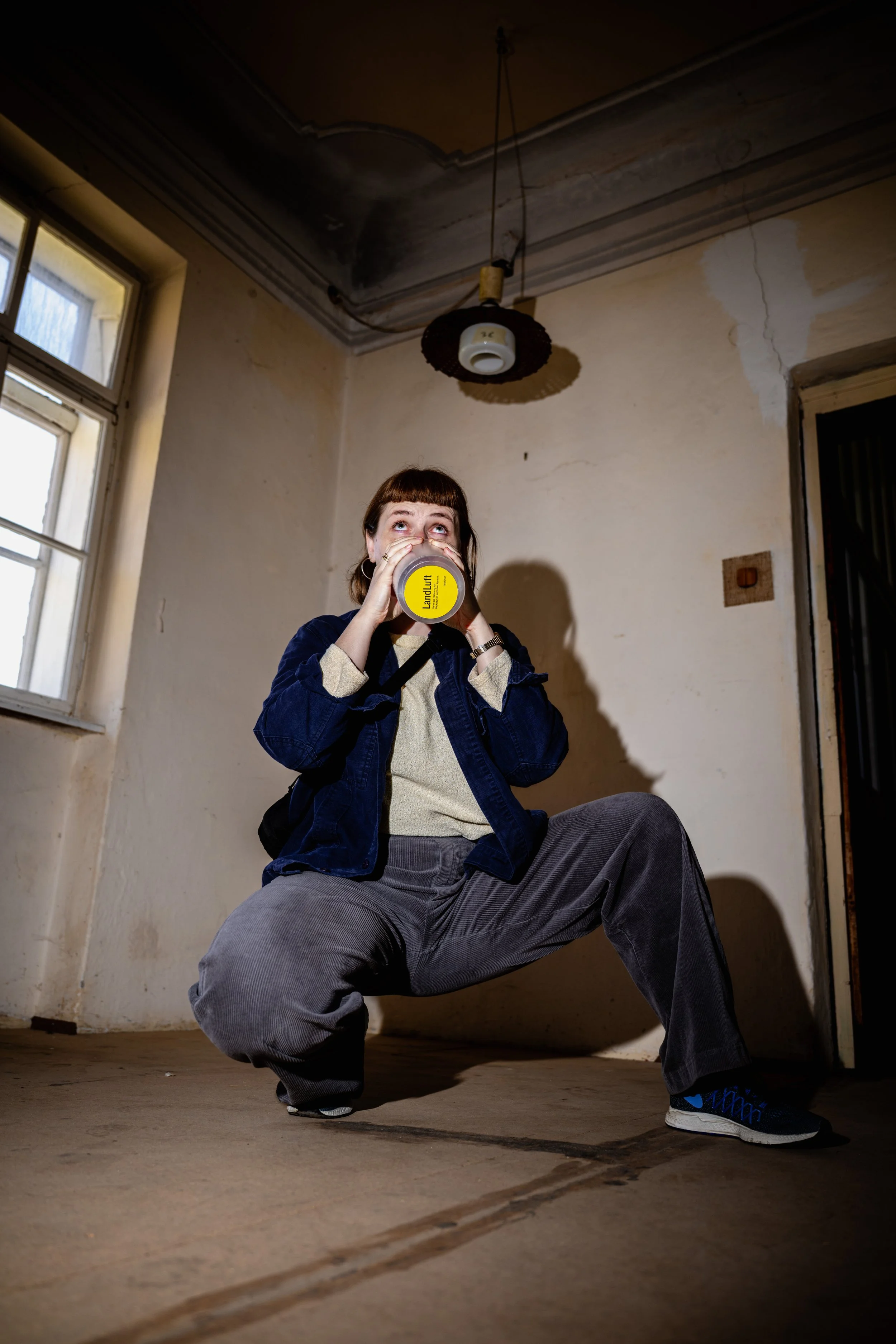 Junge Frau in einer verfallenen, leeren Wohnung, trinkt aus einer Flasche.