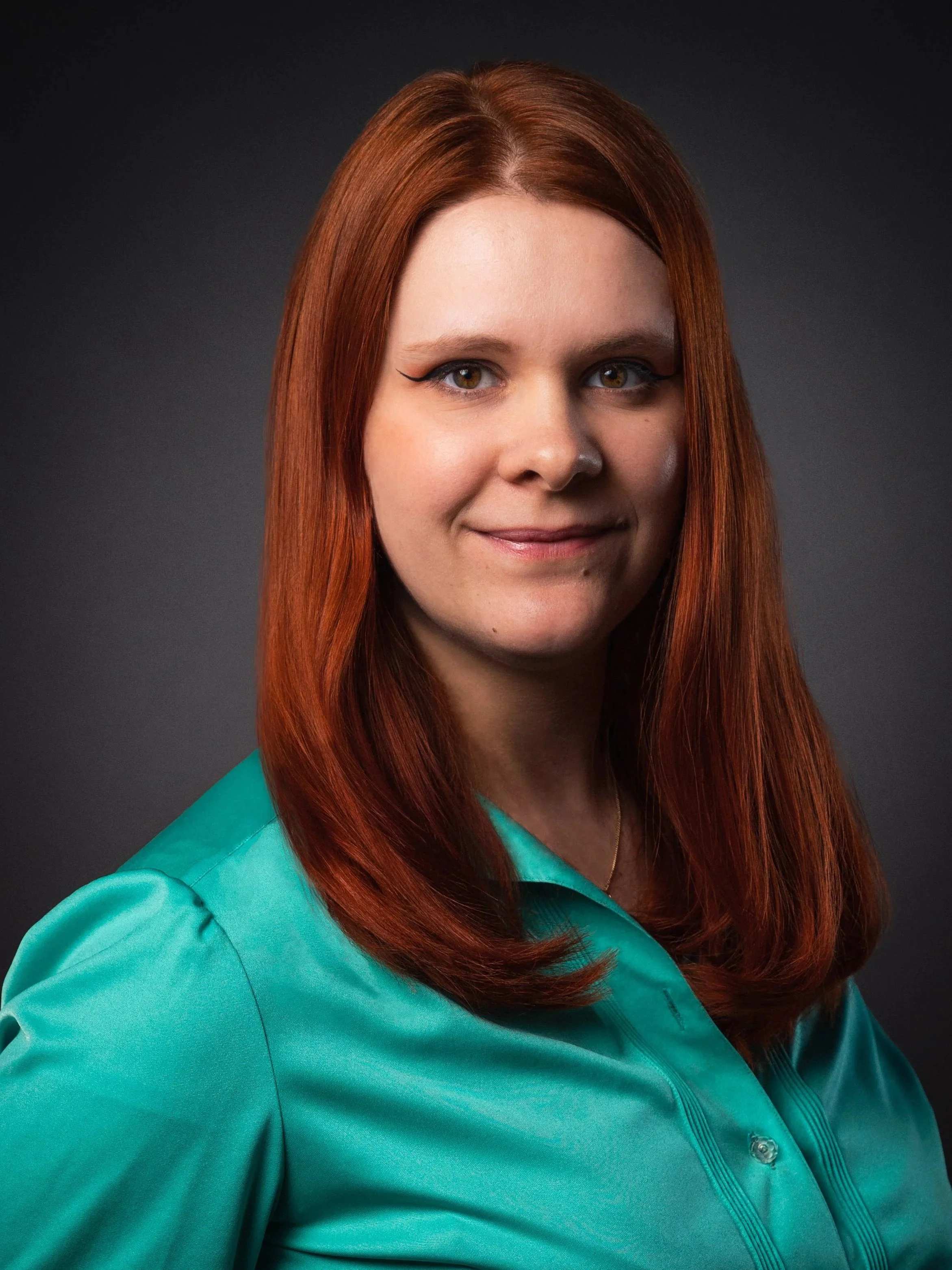 Portrait d'une femme aux cheveux roux portant une chemise turquoise, fond gris foncé