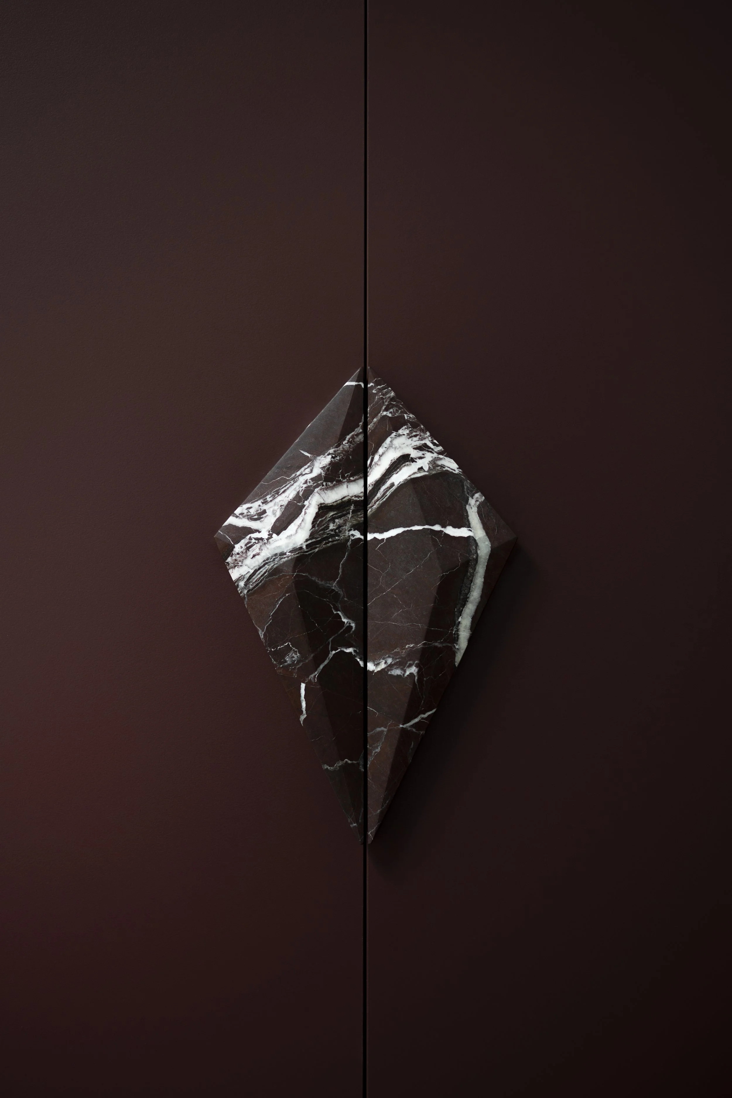 A marble pyramid with black and white veins resting on a dark brown surface, with a symmetrical composition split in the middle.