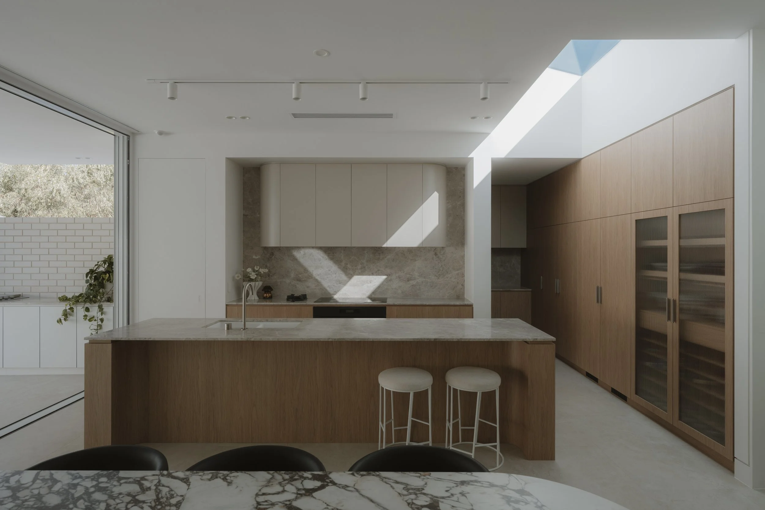 Modern kitchen with white and wood cabinetry, marble countertops, a kitchen island, and a skylight bringing in natural light.