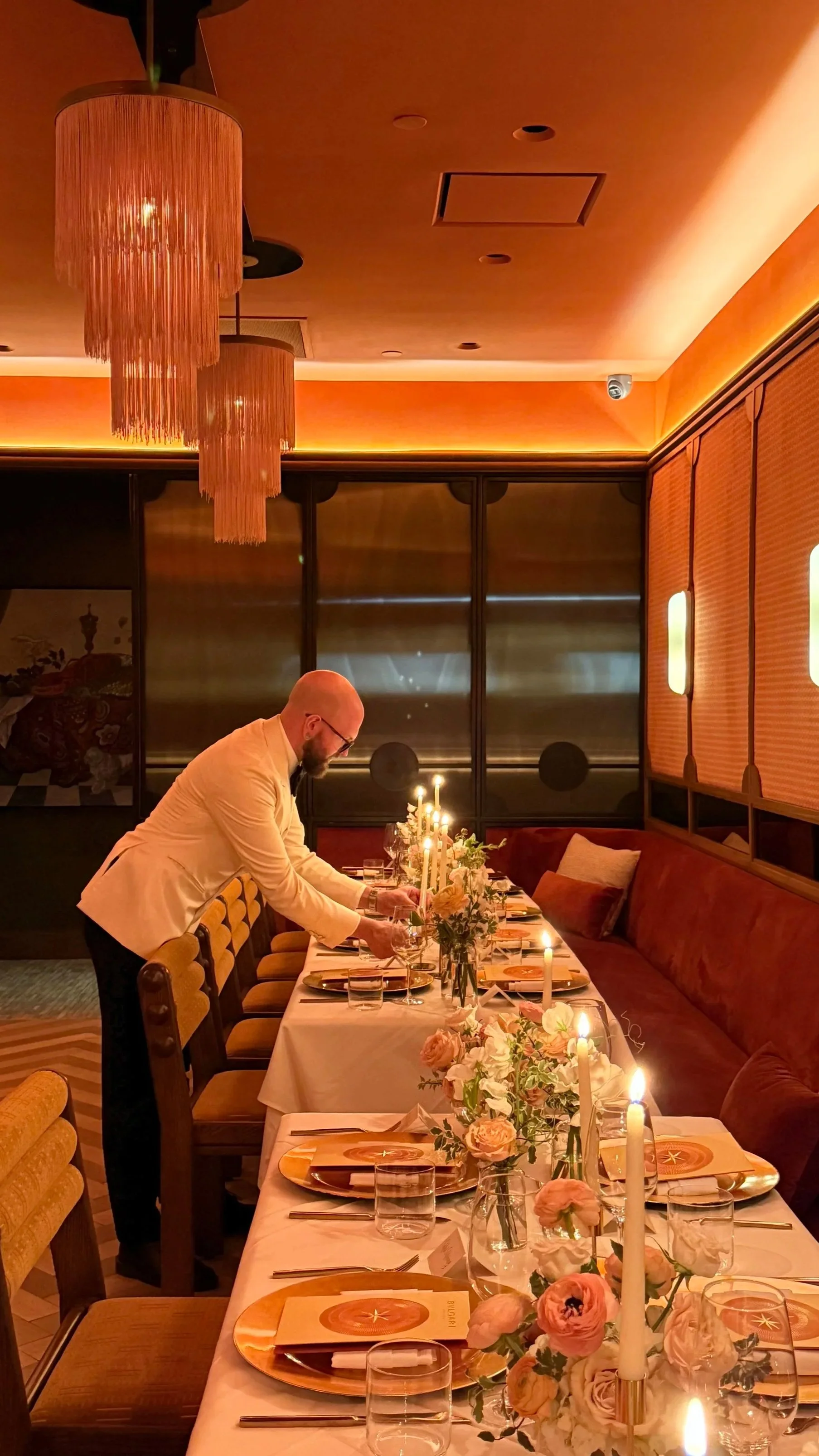 Waiter setting a candlelit tablescape with refined pastel florals for a Bulgari brand dinner, designed by The Petaler Floral & Events Co., luxury event and wedding designers for Americans in France.