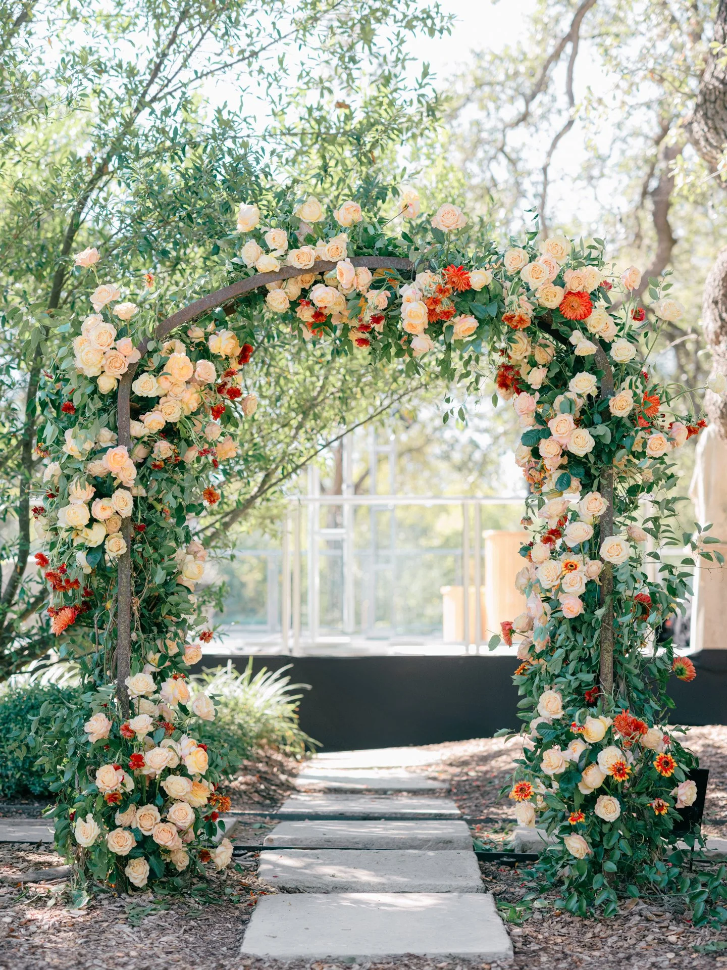 Garden-inspired wedding ceremony arch with peach roses, rust-toned blooms, and cascading greenery in an outdoor setting.