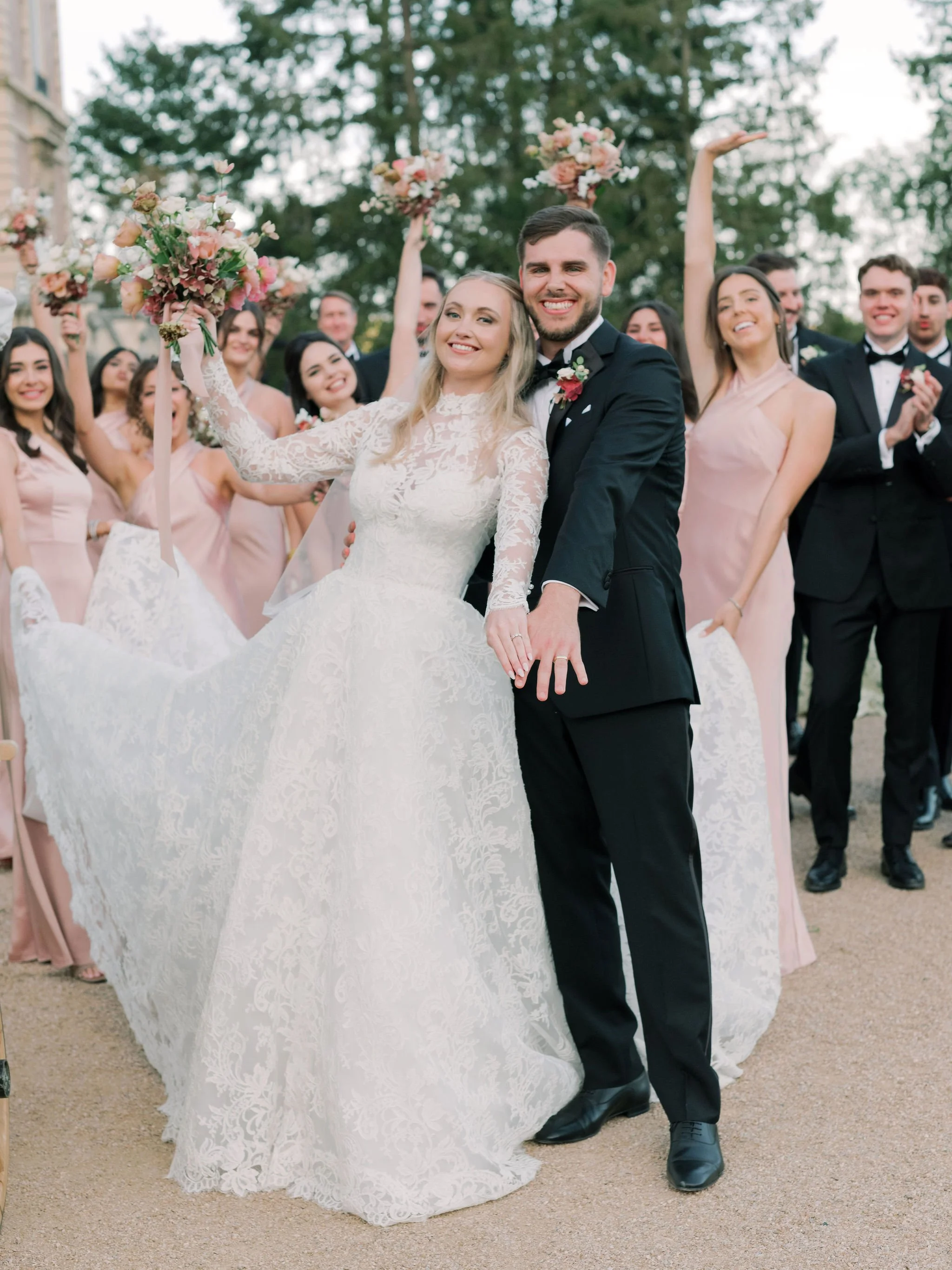 Newly married couple celebrating with their wedding party, holding up garden-style bouquets at Domaine des Halles, with florals by The Petaler Floral and Events Co., wedding planner in France.