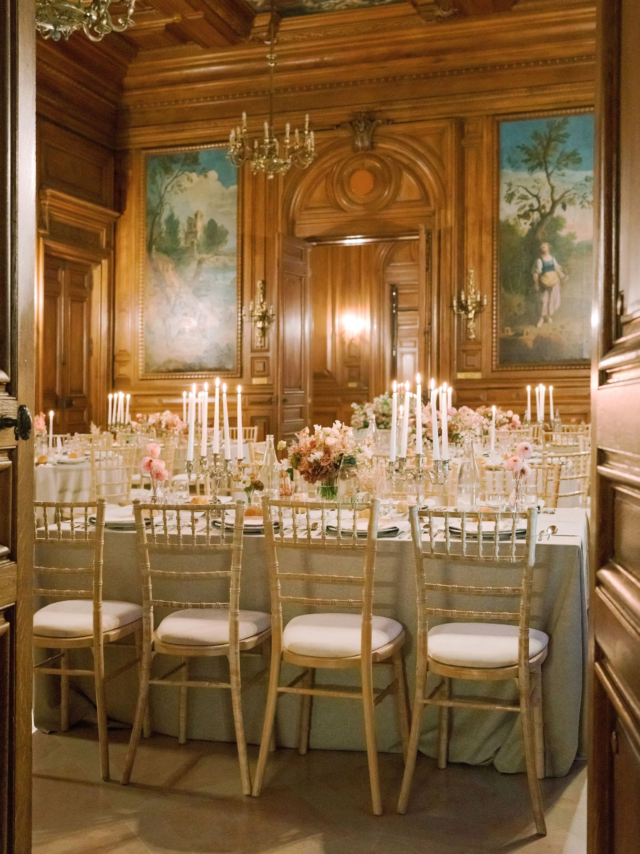 Candlelit reception in the wood-paneled salon at Domaine des Halles with romantic garden-style florals and soft taper candles, designed by The Petaler Floral and Events Co., wedding planner in France.
