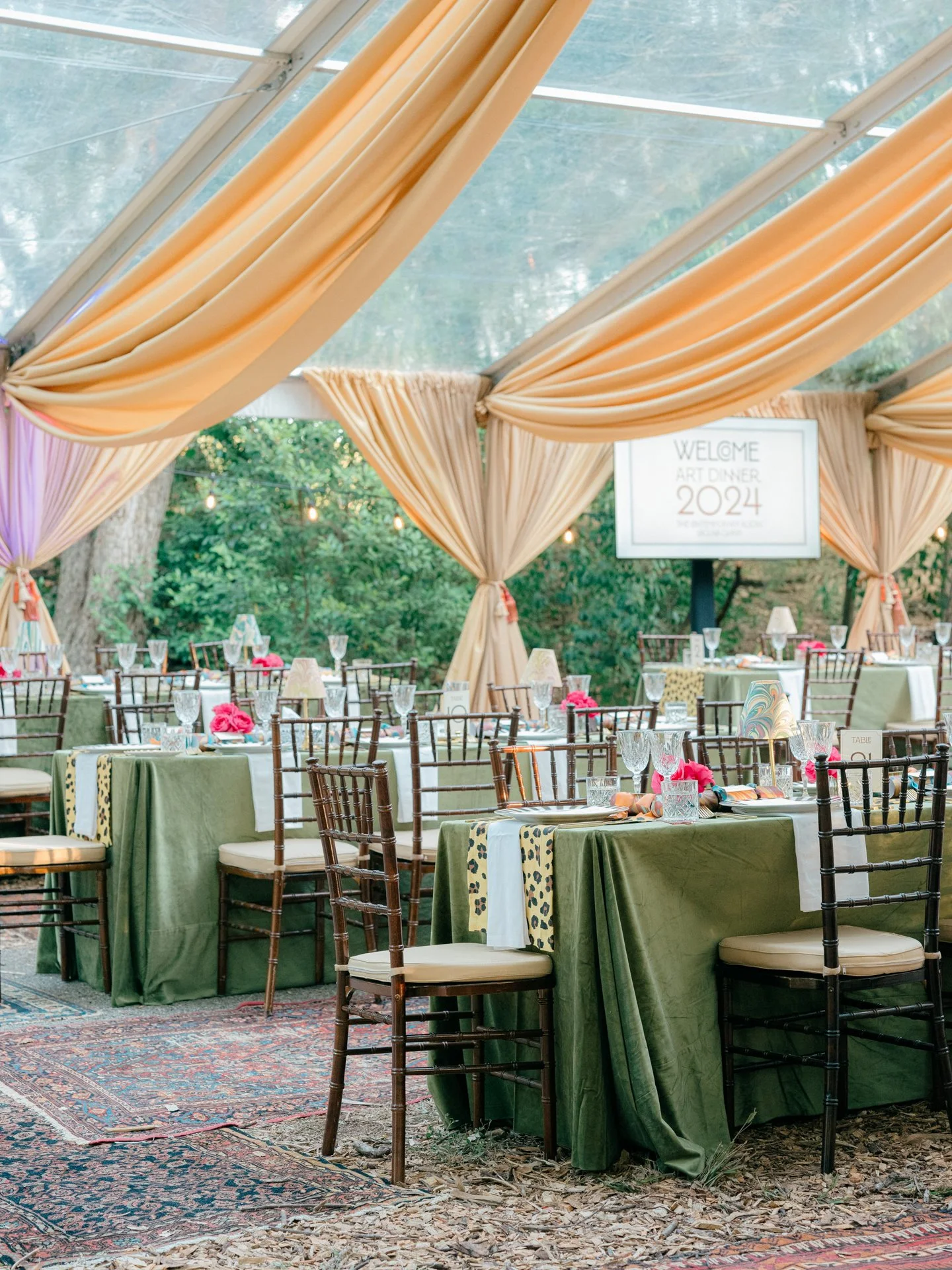 Outdoor wedding reception tables under a draped tent with contemporary garden style florals and layered tabletop design