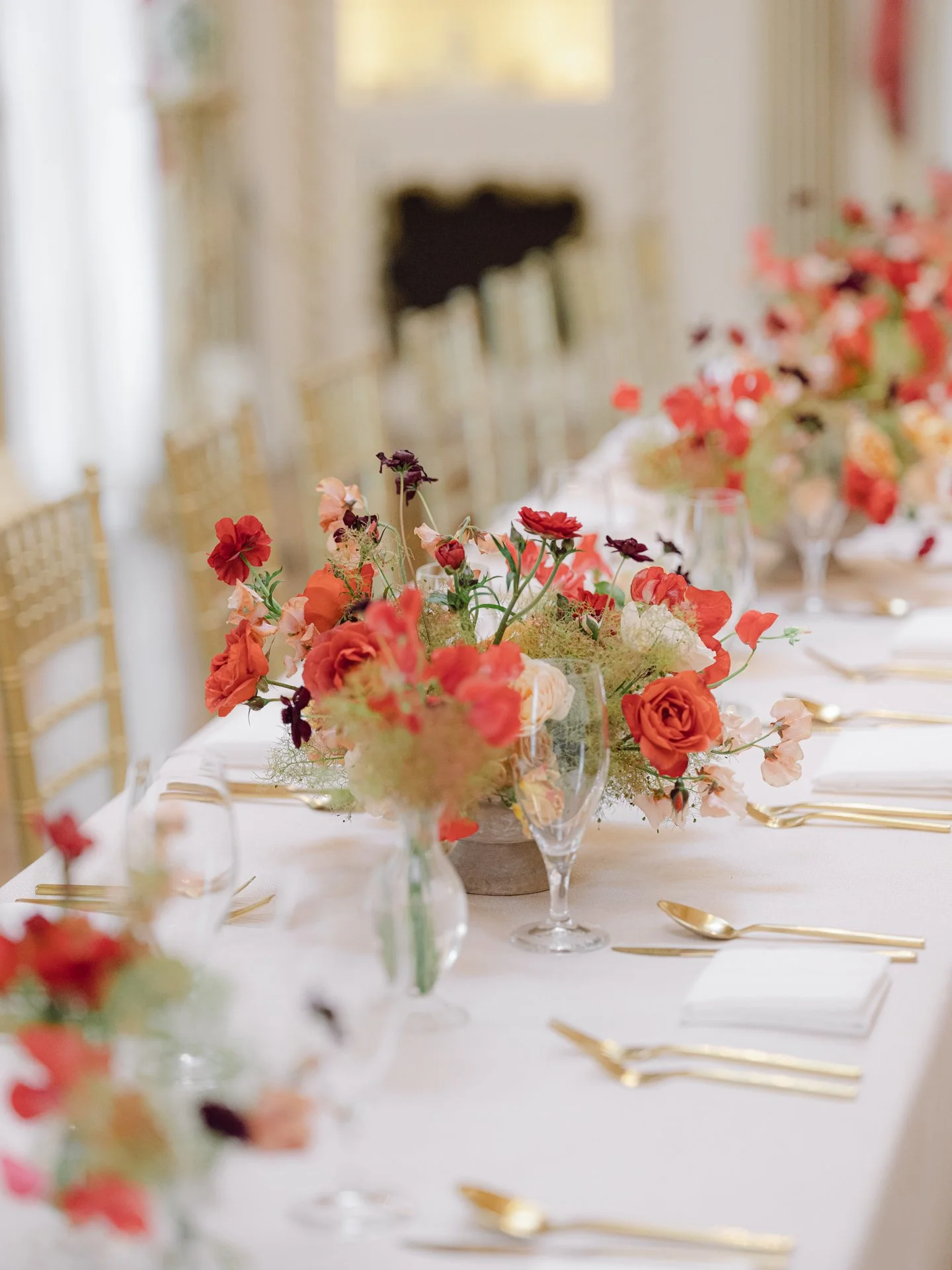 Contemporary garden-style floral centerpiece in peach and fire-engine red tones styled for fine dining at the Rienzi Museum of Decorative Arts in Houston.