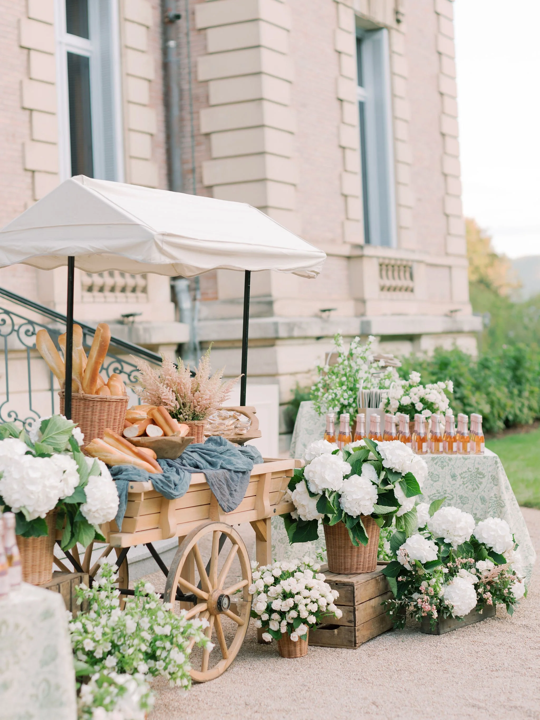 Charming welcome cart inspired by a French market with garden florals, baguettes, and individual champagne bottles at Domaine des Halles, styled by The Petaler Floral and Events Co., wedding planner in France.