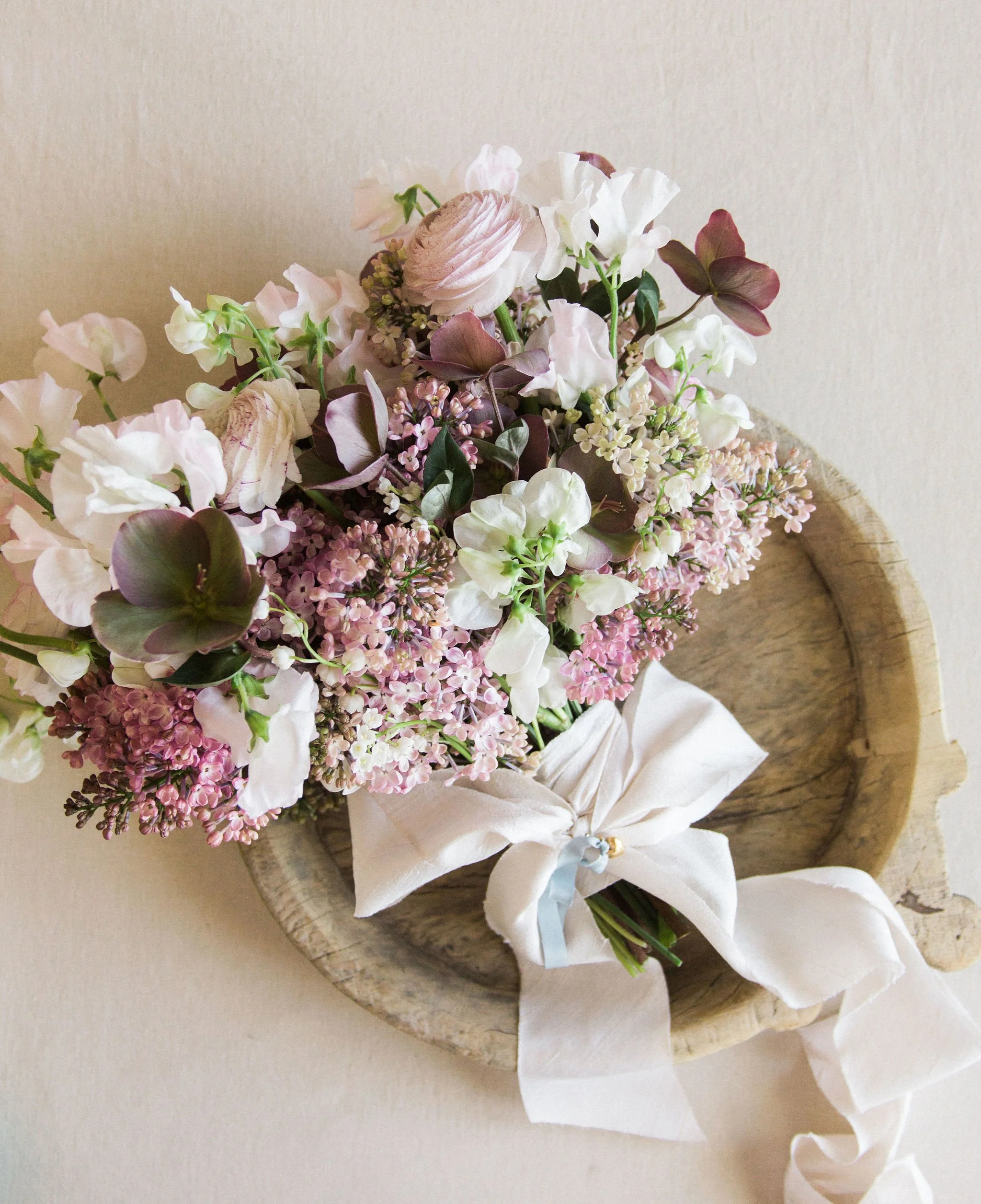 Fine-art bridal bouquet with lilac, sweet pea, and hellebore in soft mauve and ivory tones, tied with silk ribbon designed by The Petaler Floral & Events Co.