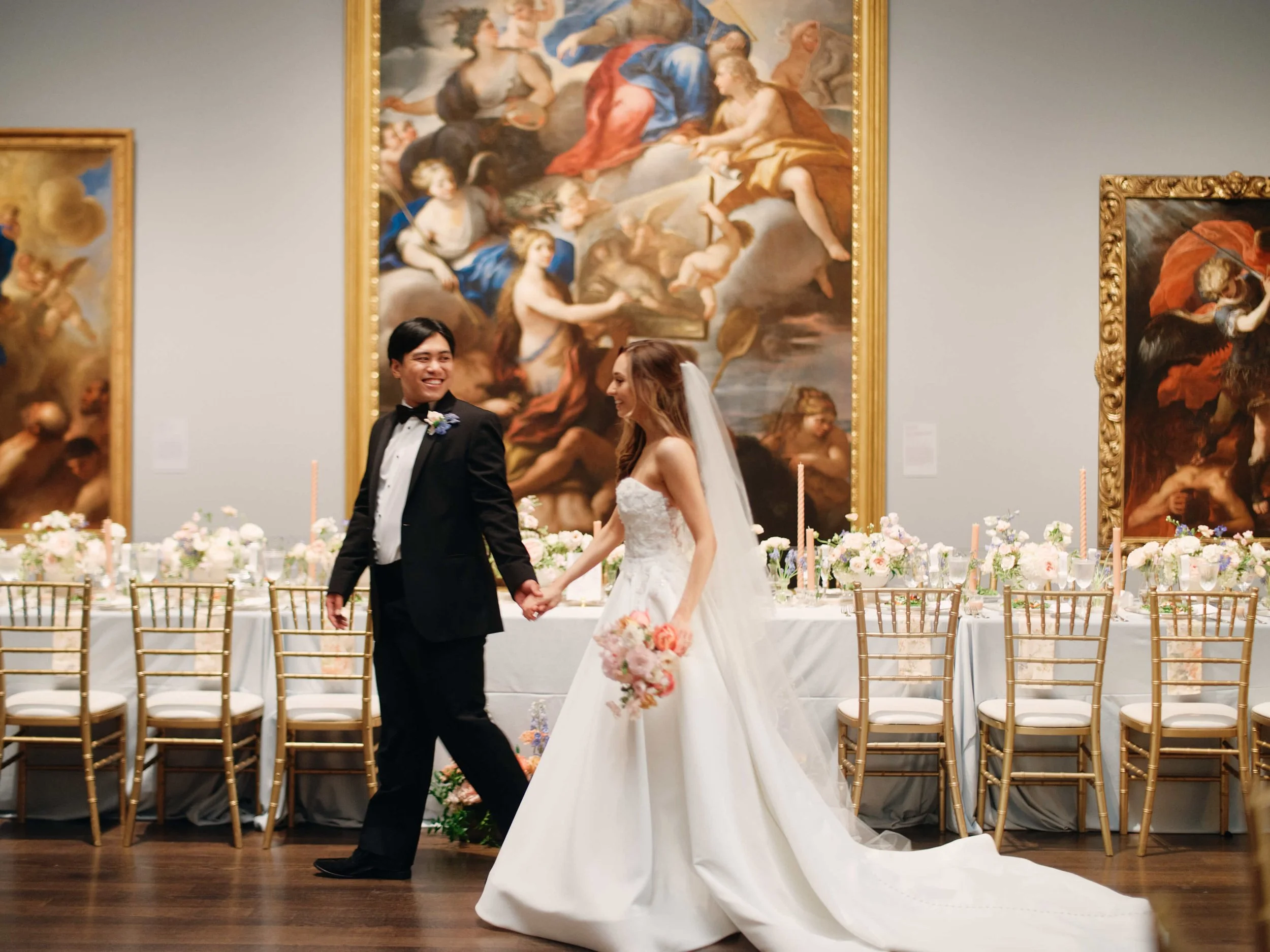 A bride and groom walk hand in hand in front of their reception table at the Museum of Fine Arts, Houston