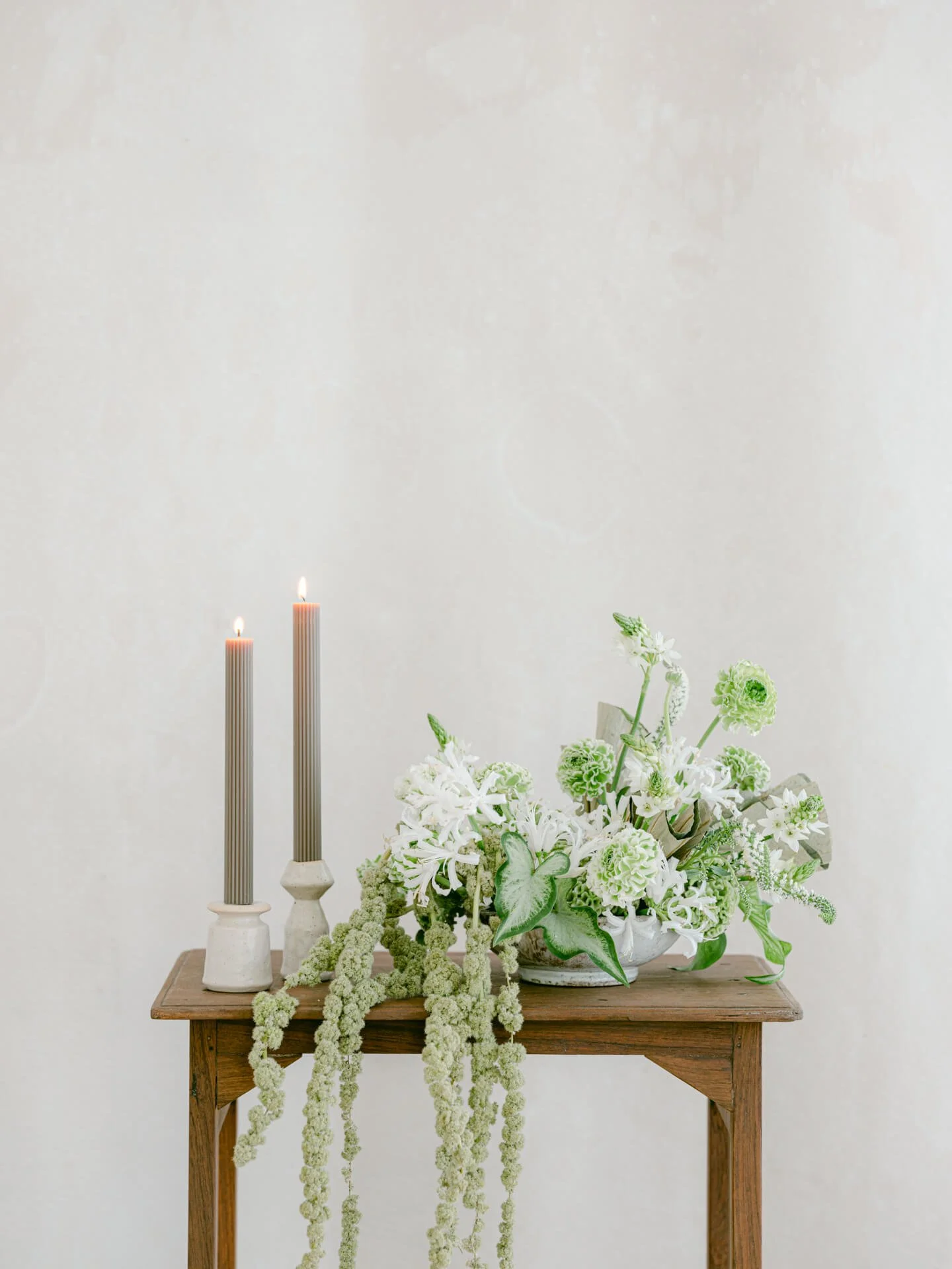 Sculptural green and white floral centerpiece with trailing botanicals and modern taper candles, styled against a soft neutral backdrop.