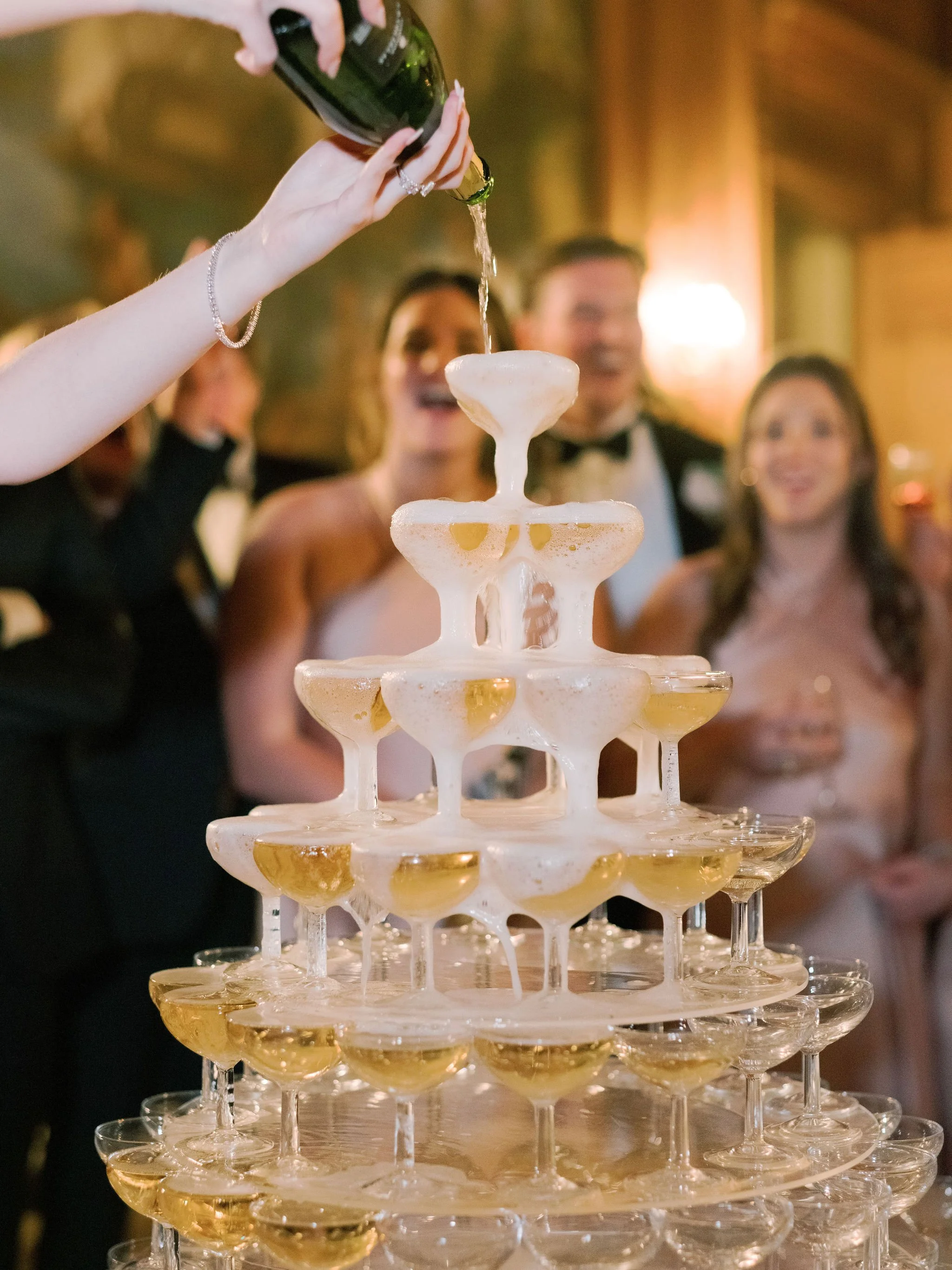 Champagne tower overflowing as guests cheer during a joyful wedding celebration at Domaine des Halles, planned and styled by The Petaler Floral and Events Co., wedding planner in France.