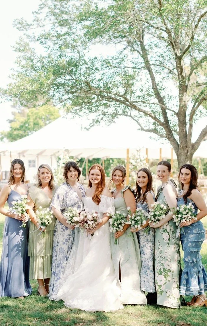 Bridesmaids in mismatched blue and green pastel dresses holding lush garden-style bouquets. Fine-art floral design for a spring coastal wedding by The Petaler Floral and Events Co.