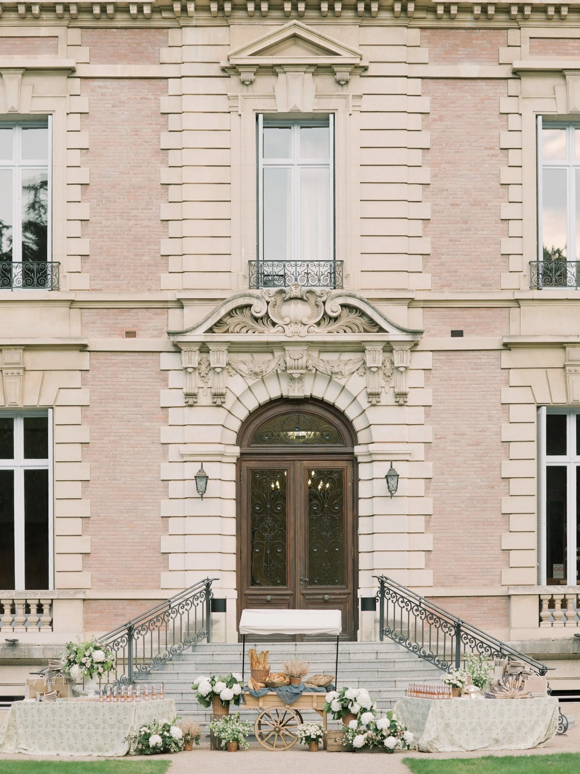 Elegant welcome display with bread cart, florals, and drinks on the steps of a French château, styled by The Petaler Floral and Events Co., wedding planner in France.