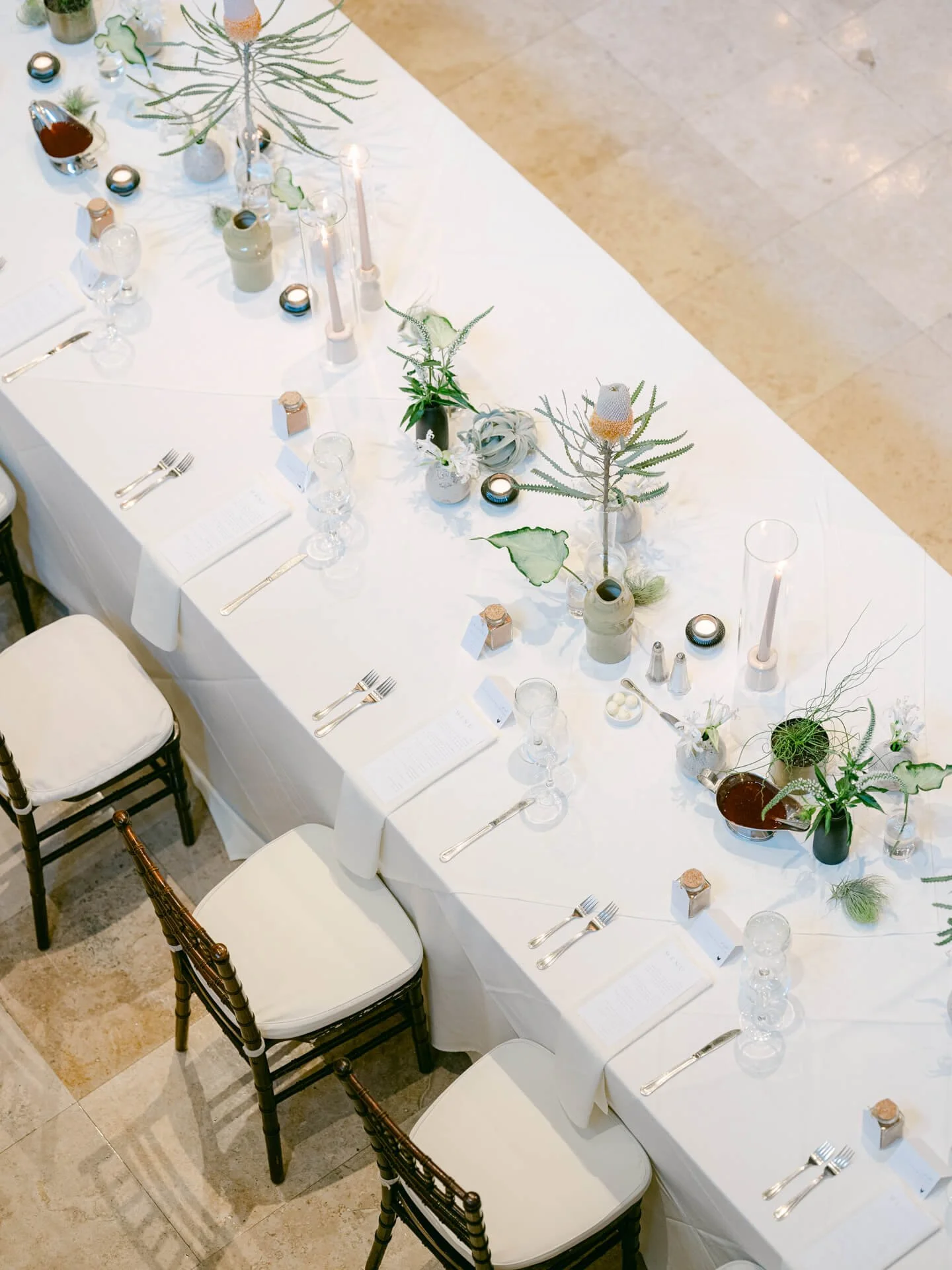 Overhead reception table design featuring restrained greenery, sculptural botanical arrangements, and crisp white linens in a contemporary wedding setting.