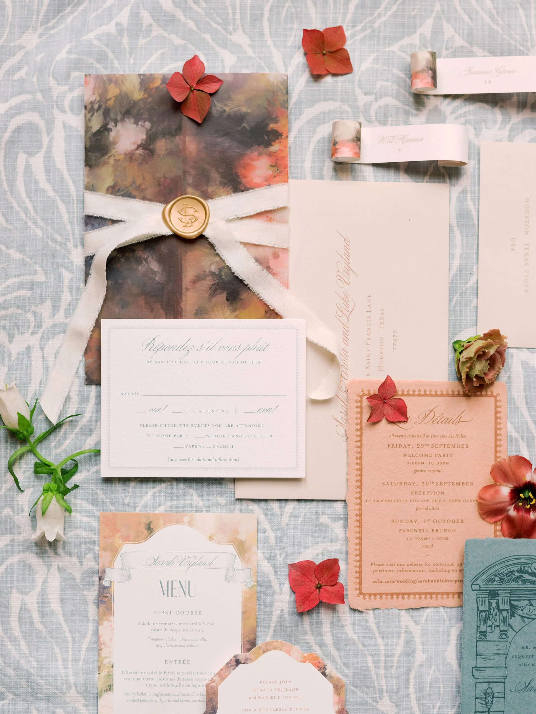 Flatlay of a romantic French wedding invitation suite with floral details and custom paper goods, styled by The Petaler Floral and Events Co., wedding planner in France.
