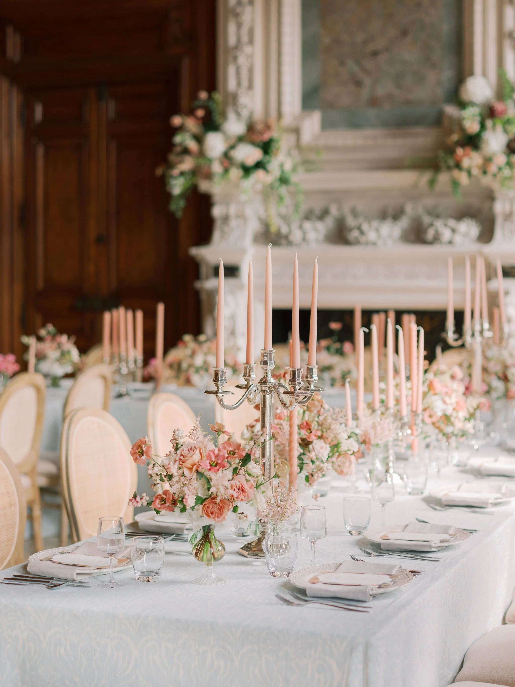 Romantic tablescape with garden-style floral arrangements and blush taper candles set for a wedding reception at Domaine des Halles, designed by The Petaler Floral and Events Co., wedding planner in France.