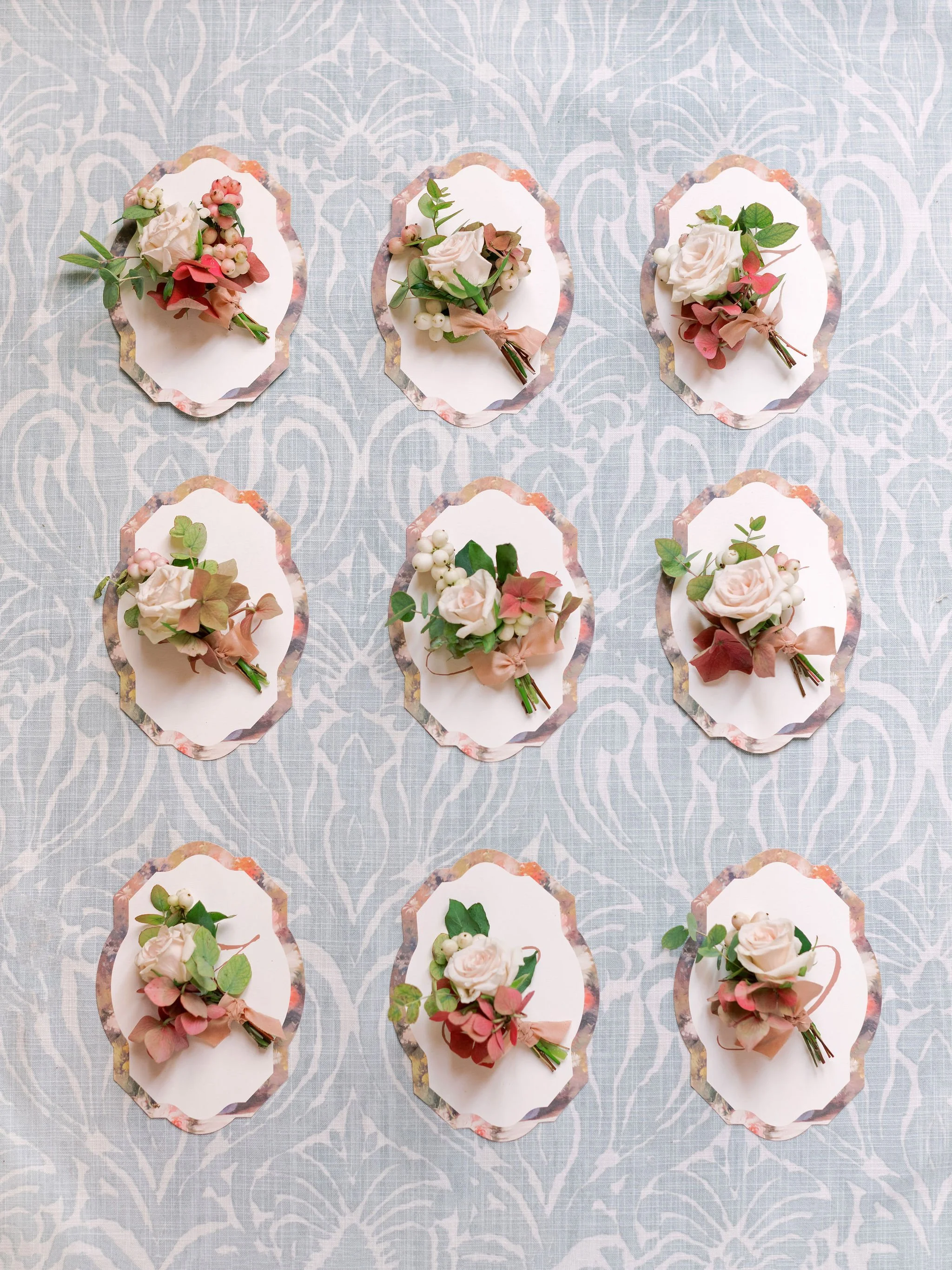 Flatlay of romantic garden-style boutonnières arranged on patterned linen at Domaine des Halles, created by The Petaler Floral and Events Co., wedding planner in France.