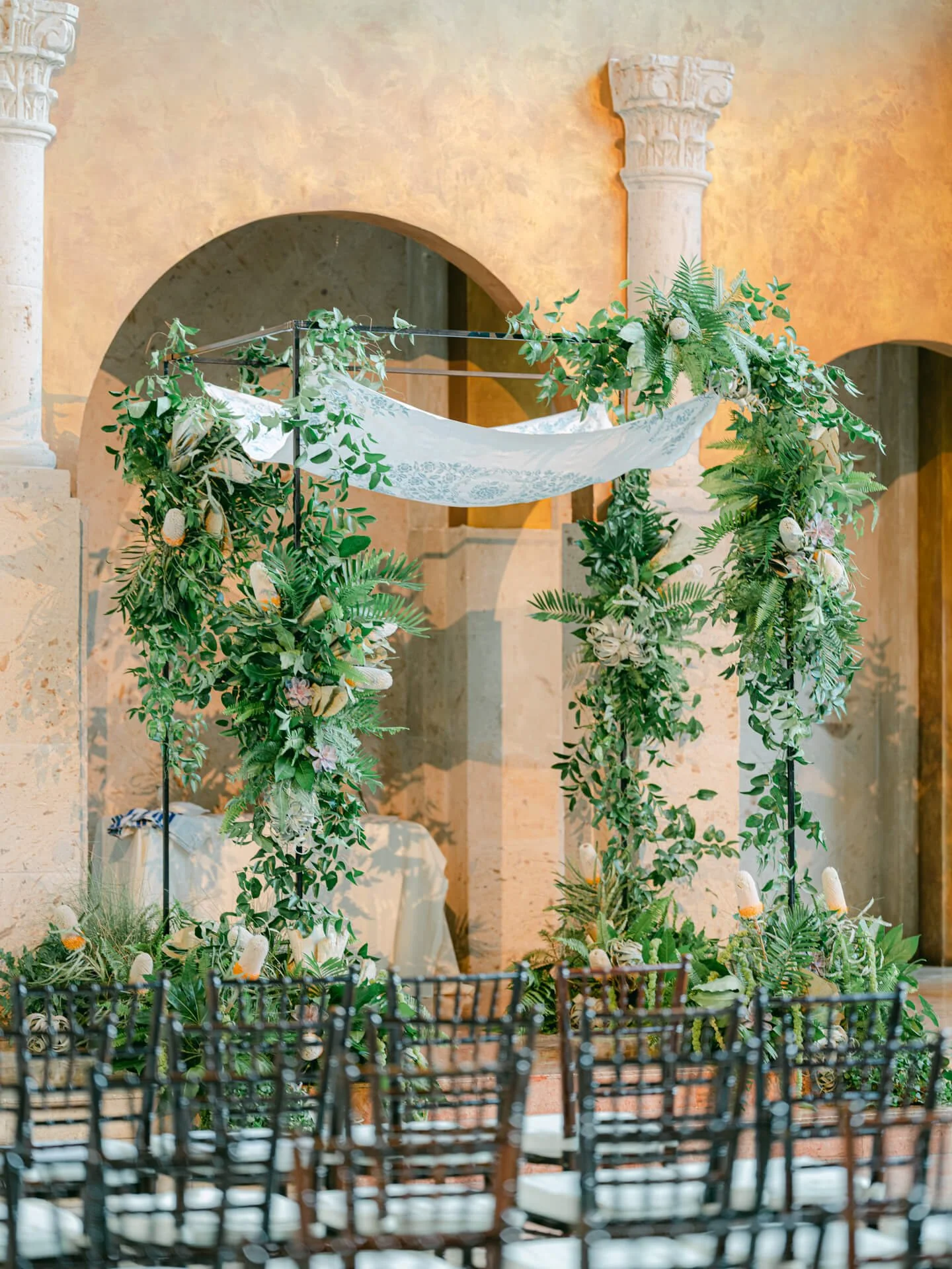 Modern chuppah installation with abundant greenery, protea accents, and refined botanical textures by The Petaler Floral and Events Co.