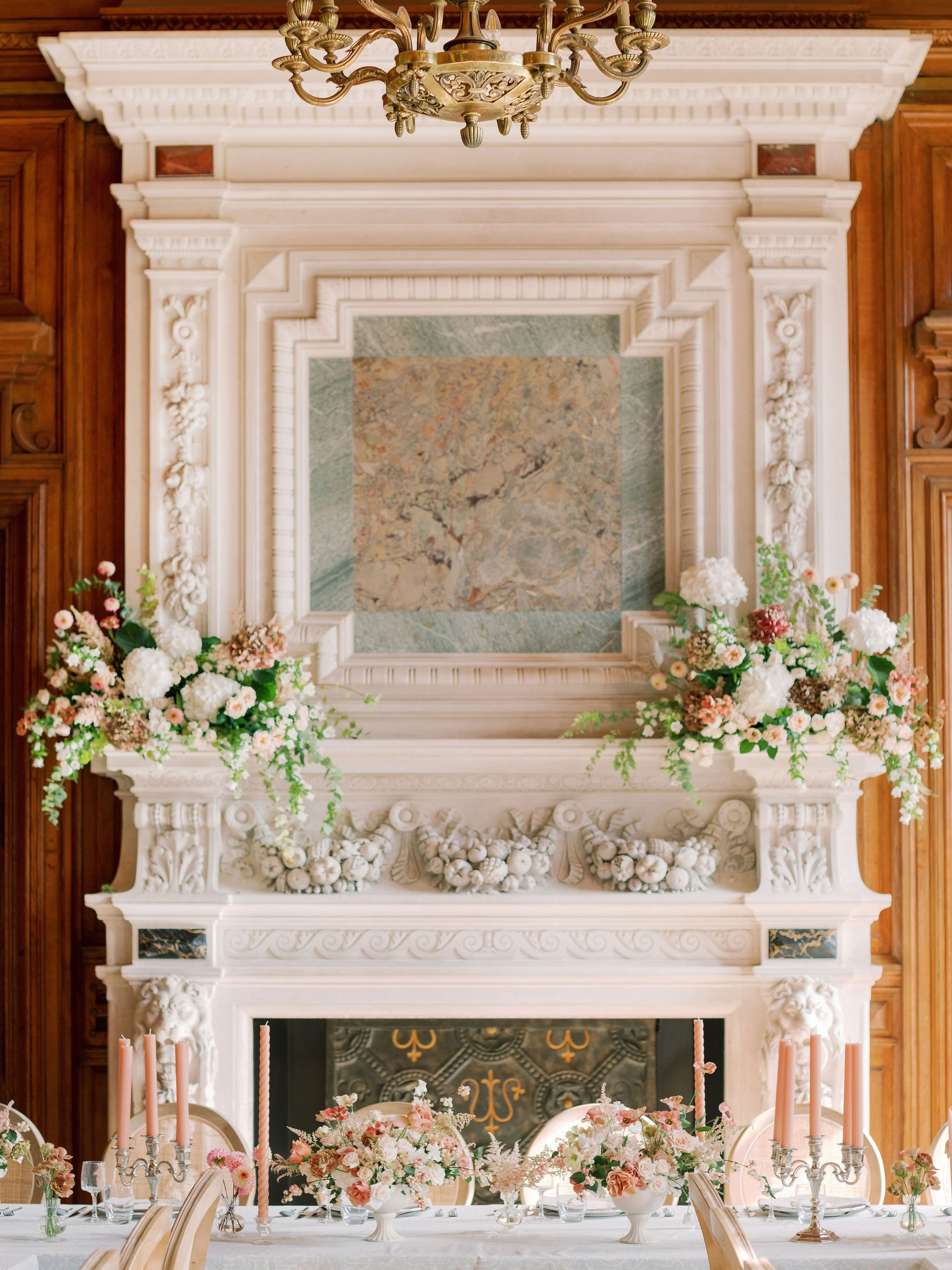 Garden-style floral arrangements and taper candles decorating an ornate fireplace and reception table at Domaine des Halles, designed by The Petaler Floral and Events Co., wedding planner in France.