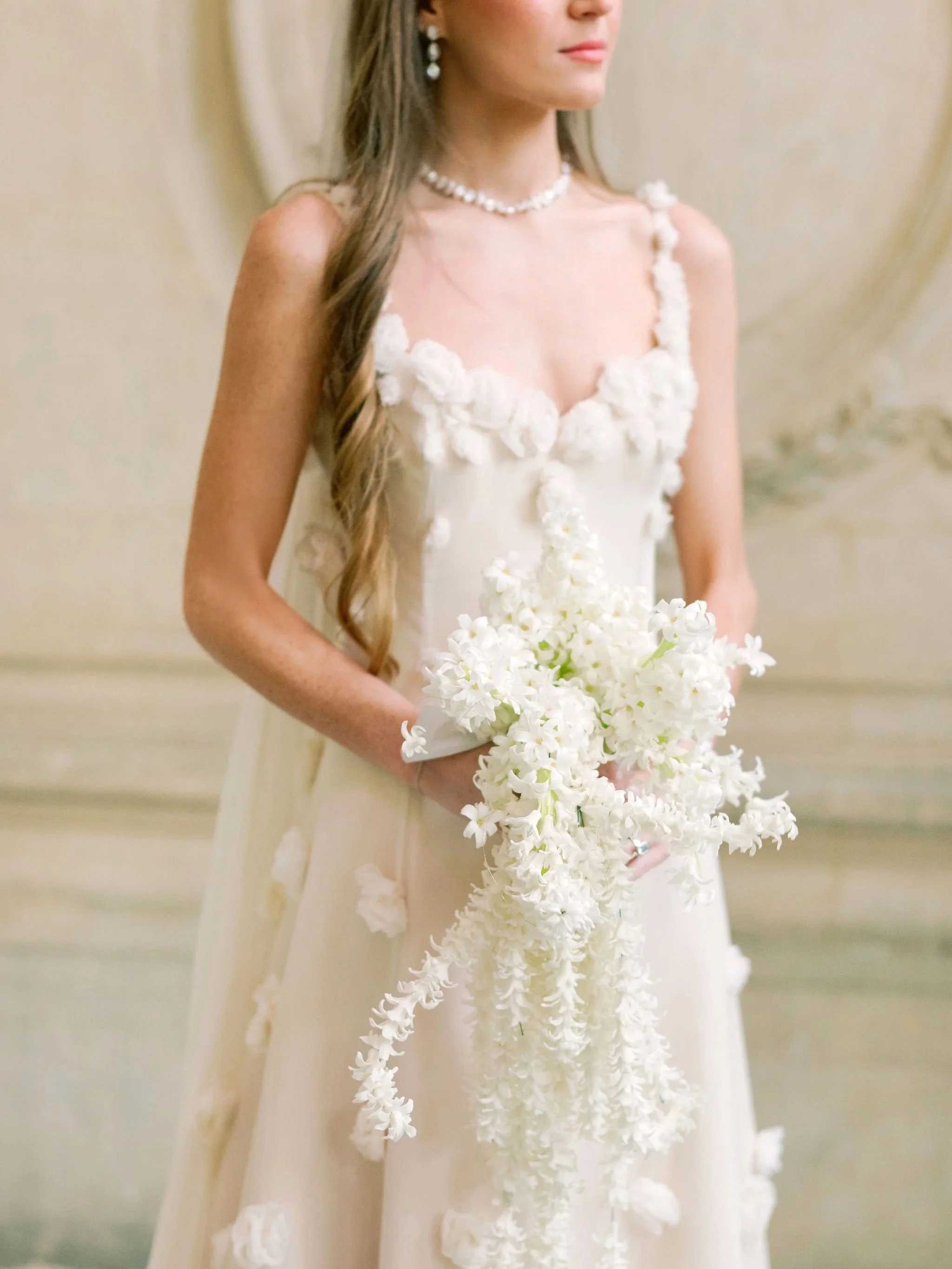 Bride in a floral-appliqué dress carrying a sculptural white bouquet of cascading hyacinths. Created by The Petaler Floral & Events Co., known for refined, art-driven florals and elevated wedding design for European weddings.