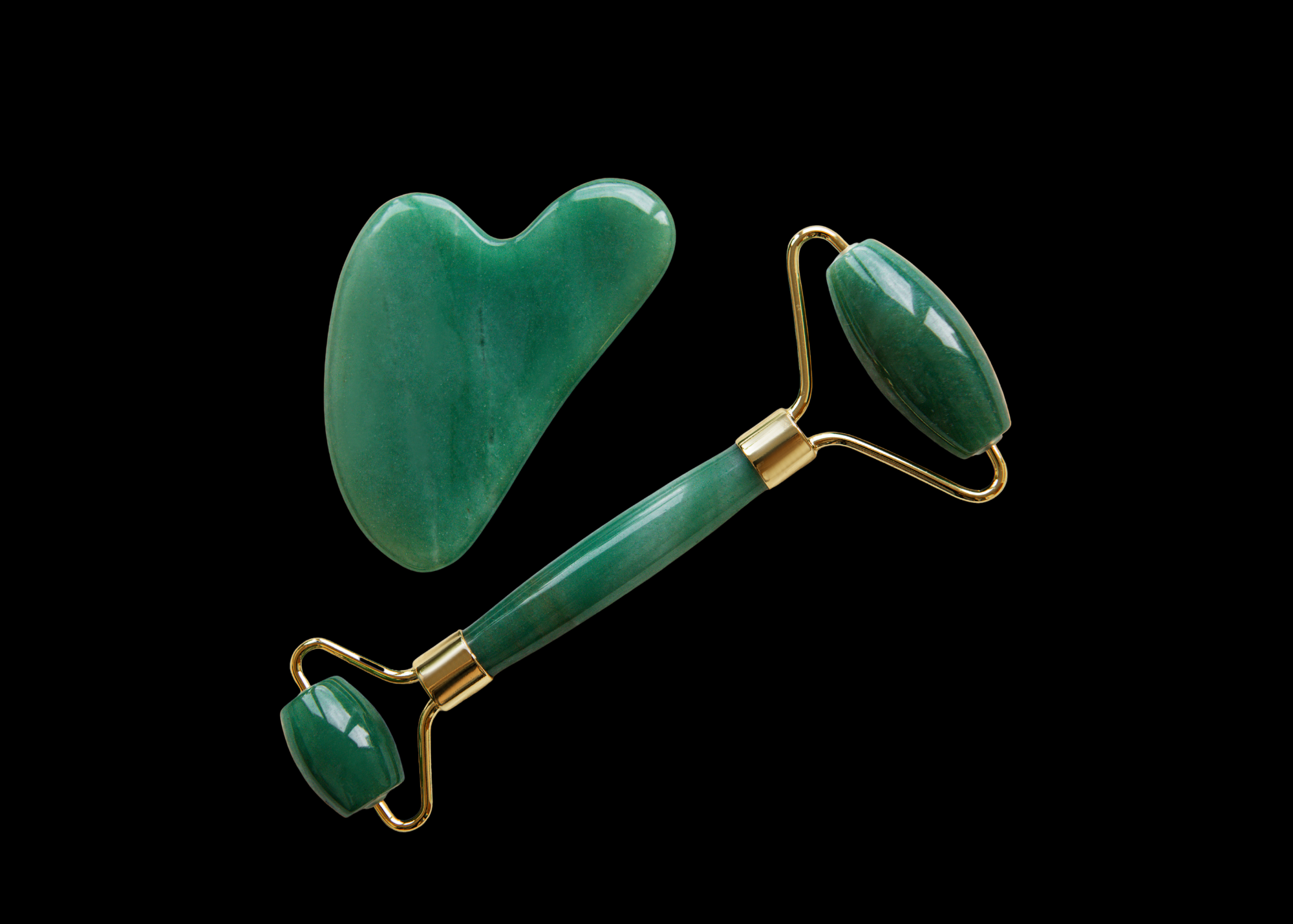 Five facial jade rollers with different colored stones arranged horizontally on a tan surface.