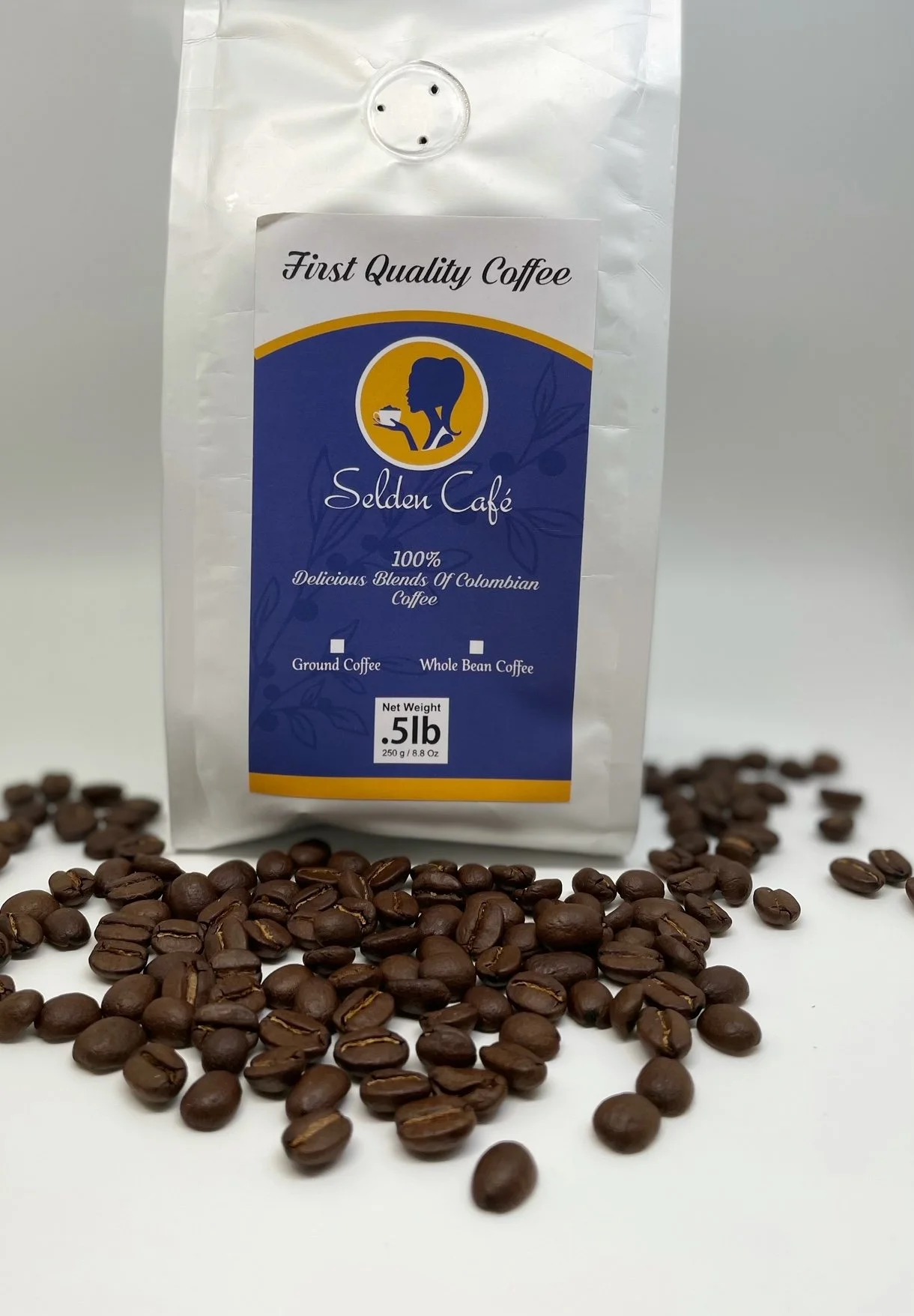 A white bag of coffee beans labeled 'Selden Café' with a blue and yellow design, surrounded by scattered coffee beans.