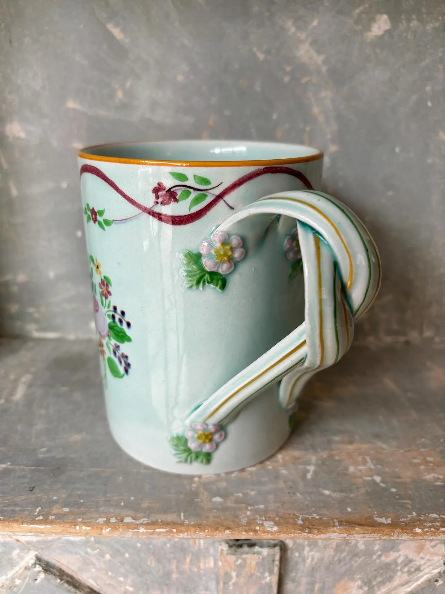 FOR SALE A beautiful, tall Calyx Ware mug by Adams, circa 1920. It is decorated with hand coloured clusters of pretty flowers with a swirling floral band around the rim. It has the most wonderful and very unusual handle made up of two intertwined rib
