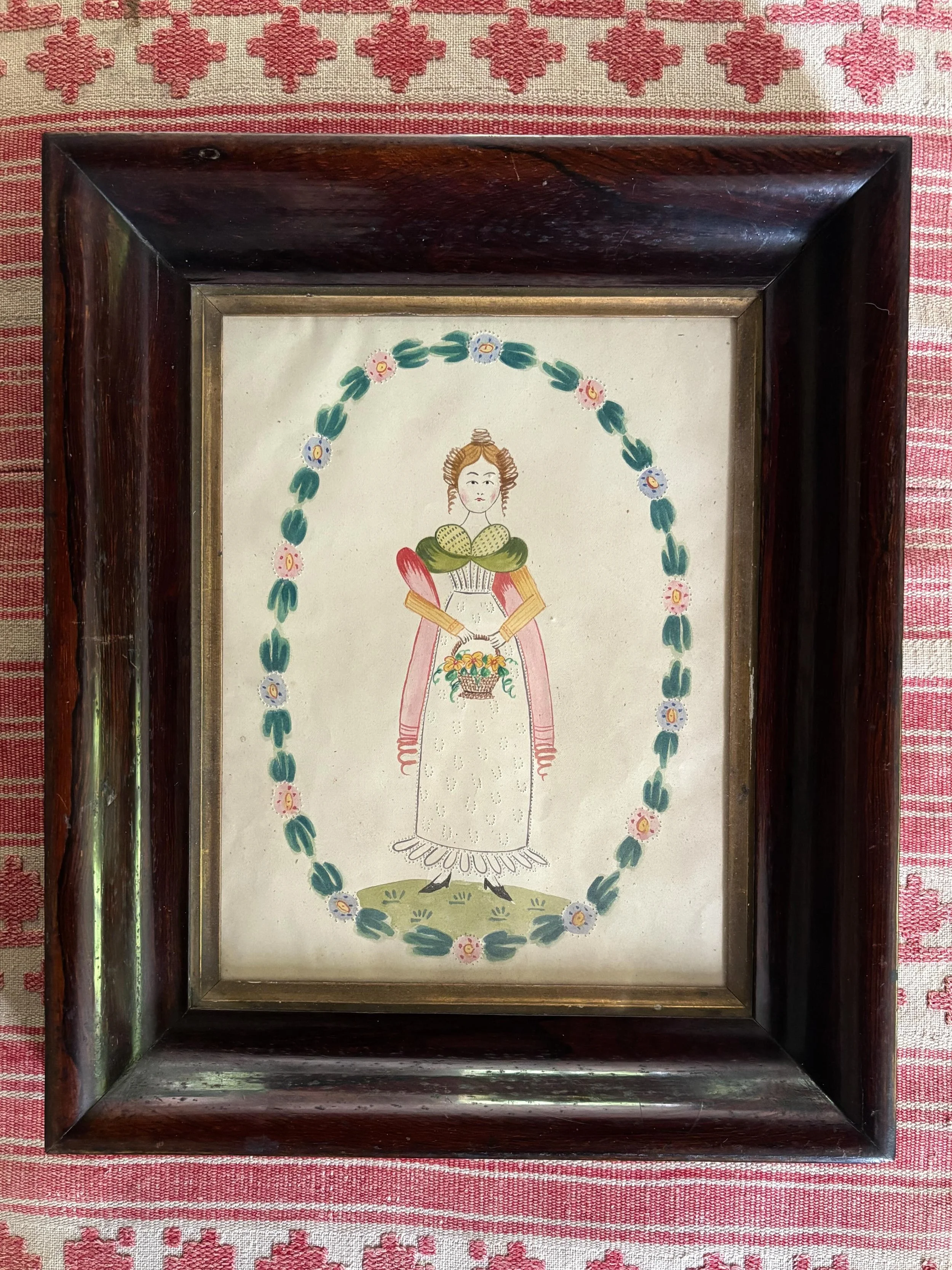FOR SALE An enchanting 19th century folk art watercolour painting of a young lady holding a basket of flowers. It has been decorated with tiny pinpricks to her skirt and bodice and around each of the flowers in the garland that surrounds her. 

It is
