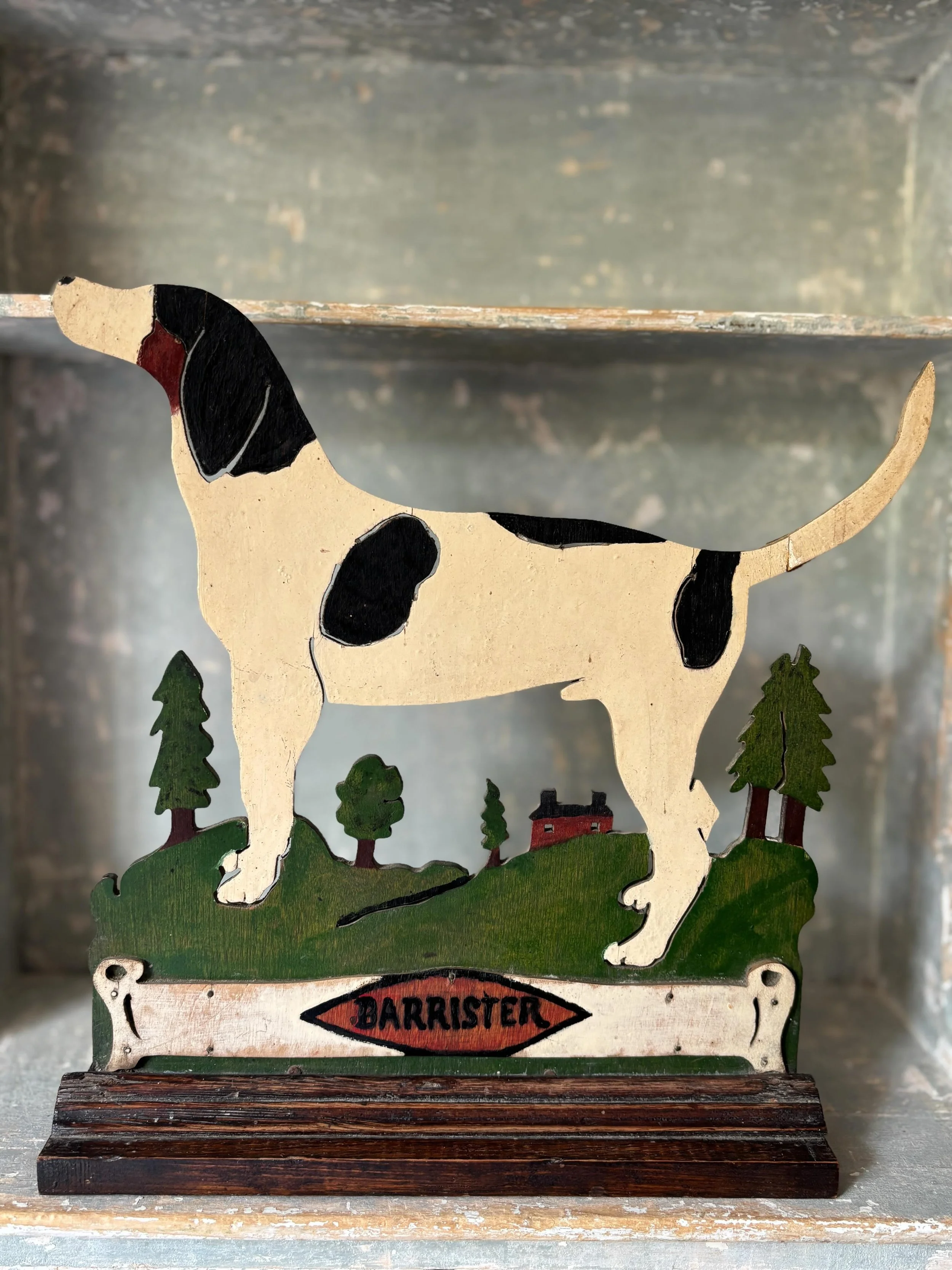 FOR SALE A vintage folk art cut wood silhouette of a hound against a rural backdrop. Circa 1940-1960. Lovely primitive colours and what a splendid pose!

The name &lsquo;Barrister&rsquo; (surely a perfect name for this distinguished subject) is inscr