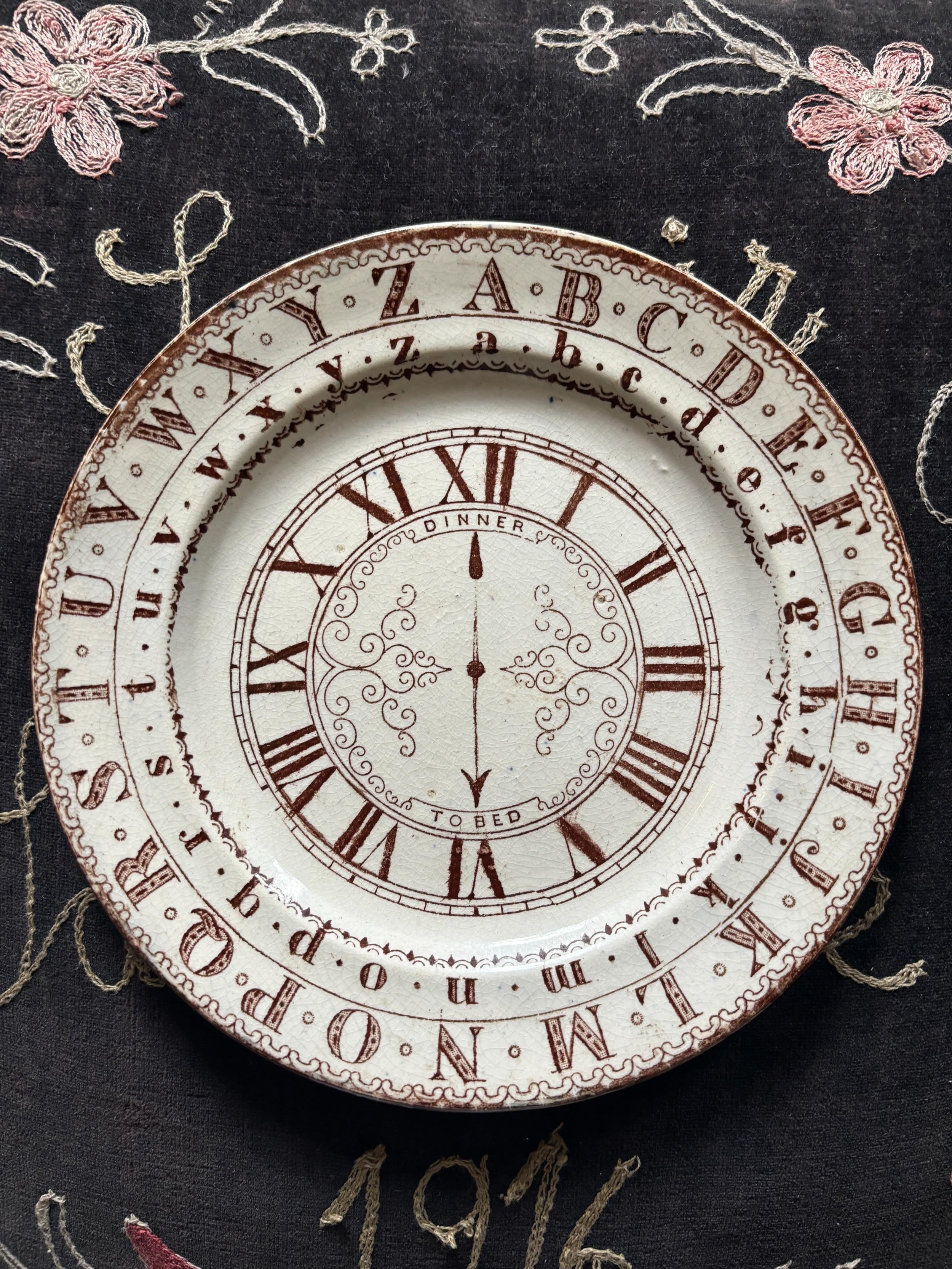 FOR SALE An antique Staffordshire pottery nursery plate, early to mid 19th century, brown transfer printed. The hands of the clock point to &lsquo;Dinner&rsquo; and &rsquo;To Bed&rsquo;, the Roman numerals and encircling alphabets signalling its educ