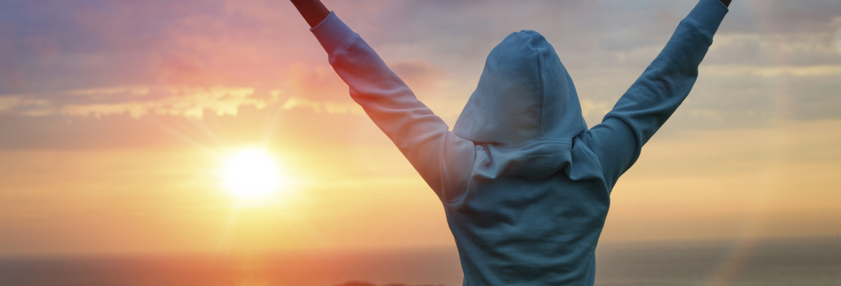 Person raising arms facing into the sunrise