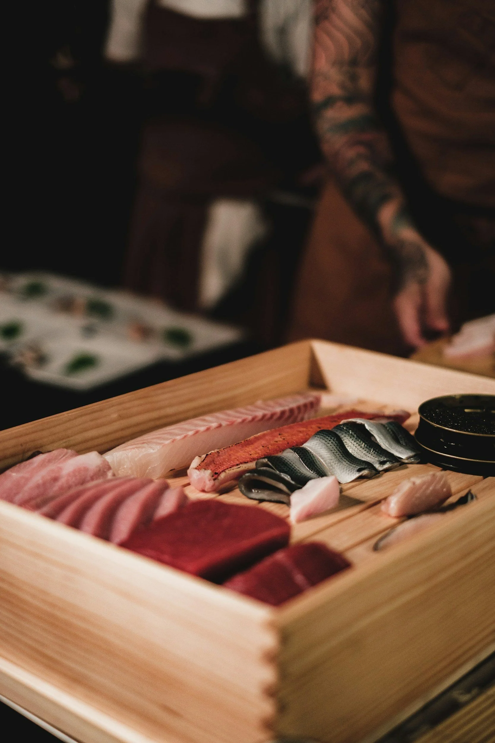 An assortment of raw fish and seafood, including slices of tuna, salmon, and other fish, arranged on a wooden sushi tray.