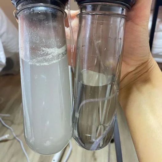 Two glass test tubes held by a hand, one with a white cloudy liquid and the other with a clear liquid, connected by tubes inside the test tubes.