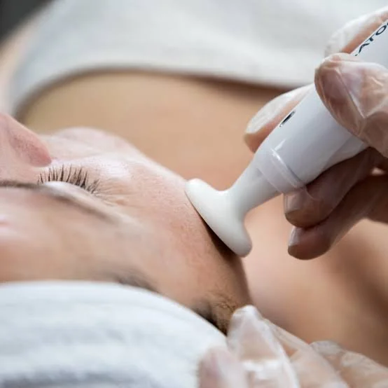 A person receiving a facial ultrasound treatment on their face from a technician wearing gloves.