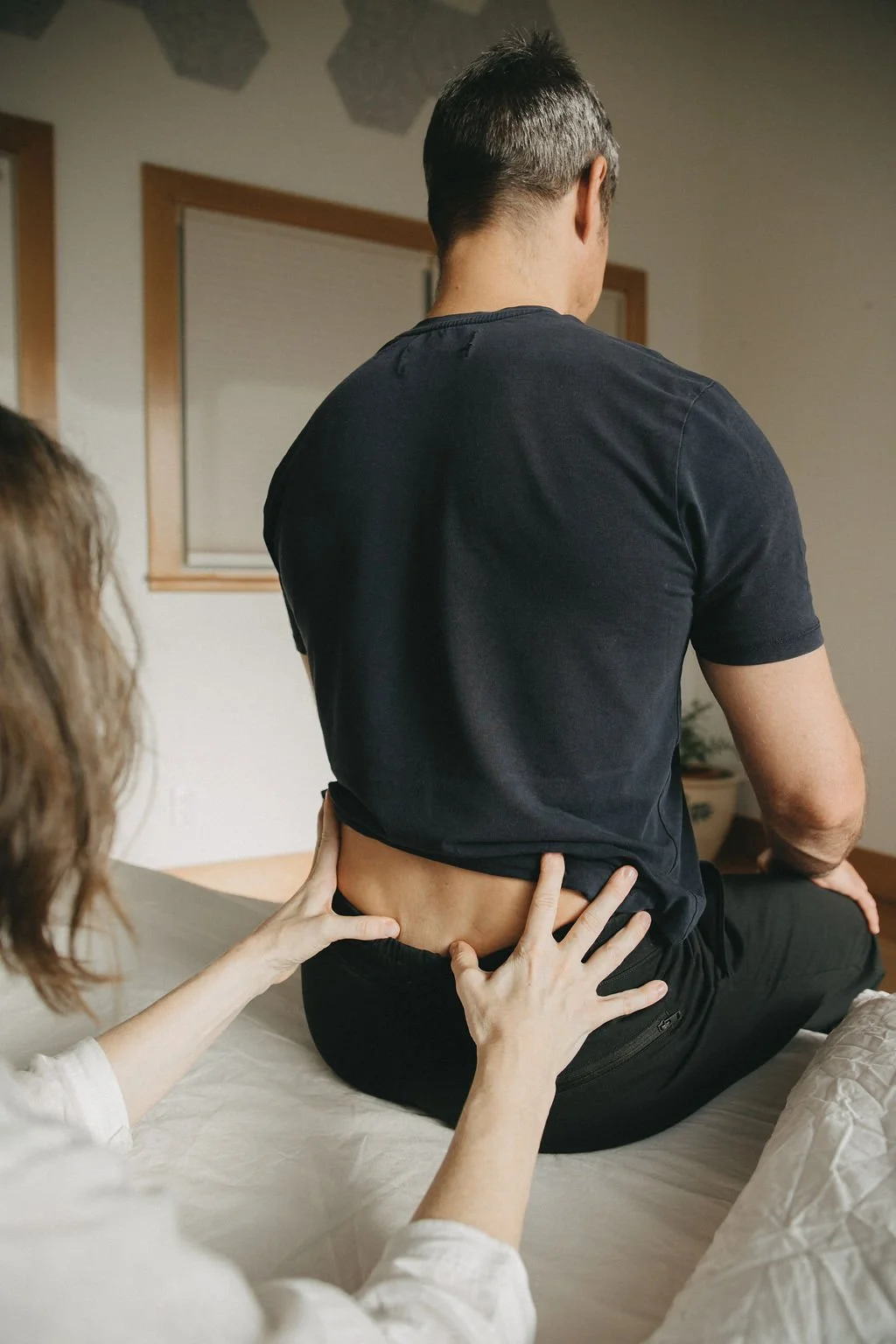 A woman with braided hair and a baby sitting on her lap, facing another woman at a desk. The woman at the desk has red hair and is using a computer. A colorful skull model and framed artwork are on the desk. The scene appears to be in a medical or therapy office.