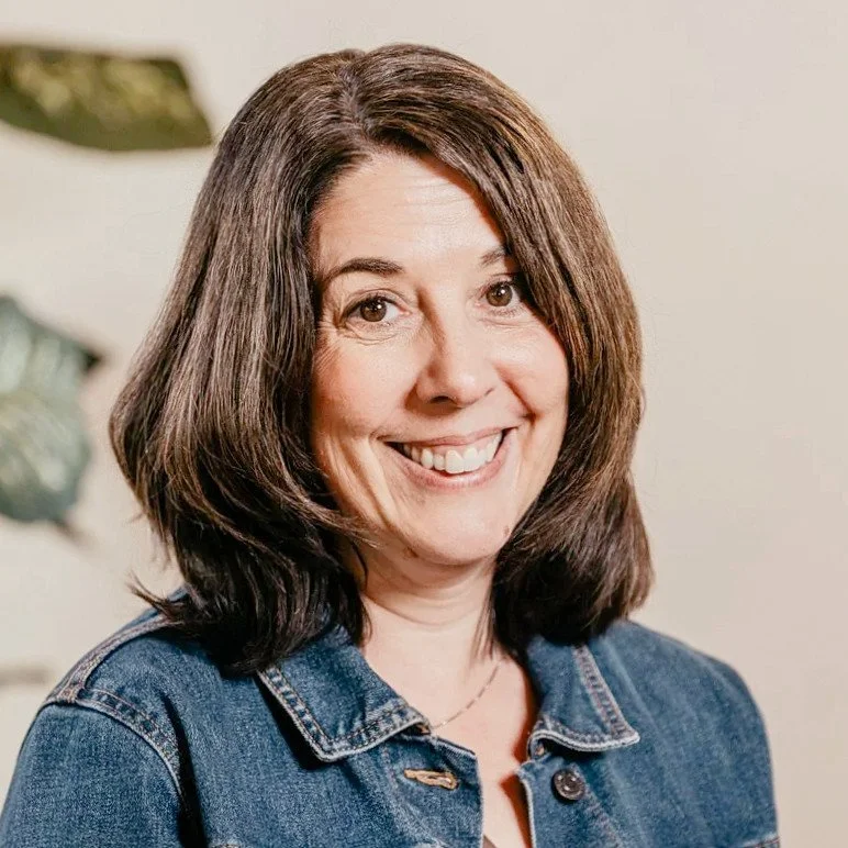 Smiling woman in denim jacket near a plant