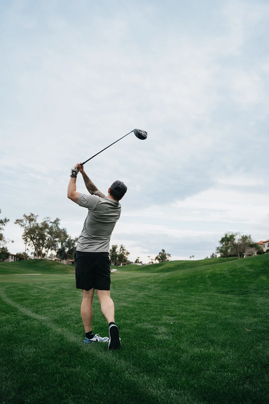 A man on a golf course swinging a golf club during daytime under cloudy sky.