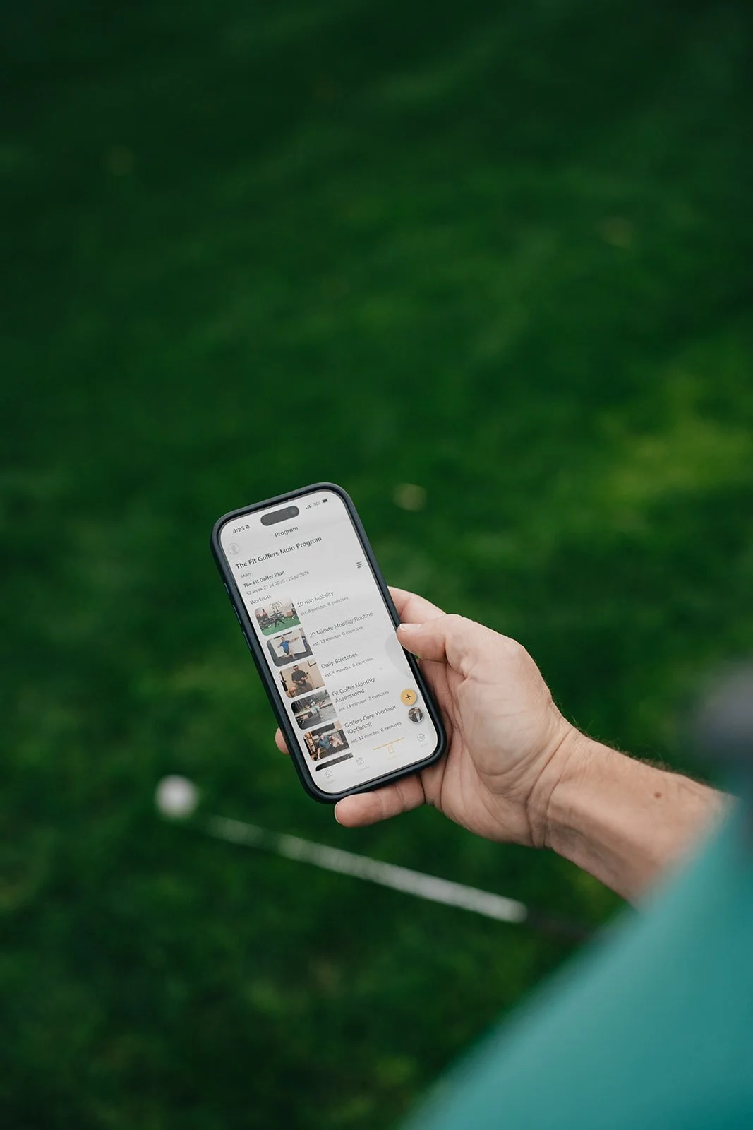 A person holding a smartphone displaying a fitness program app on a golf course.