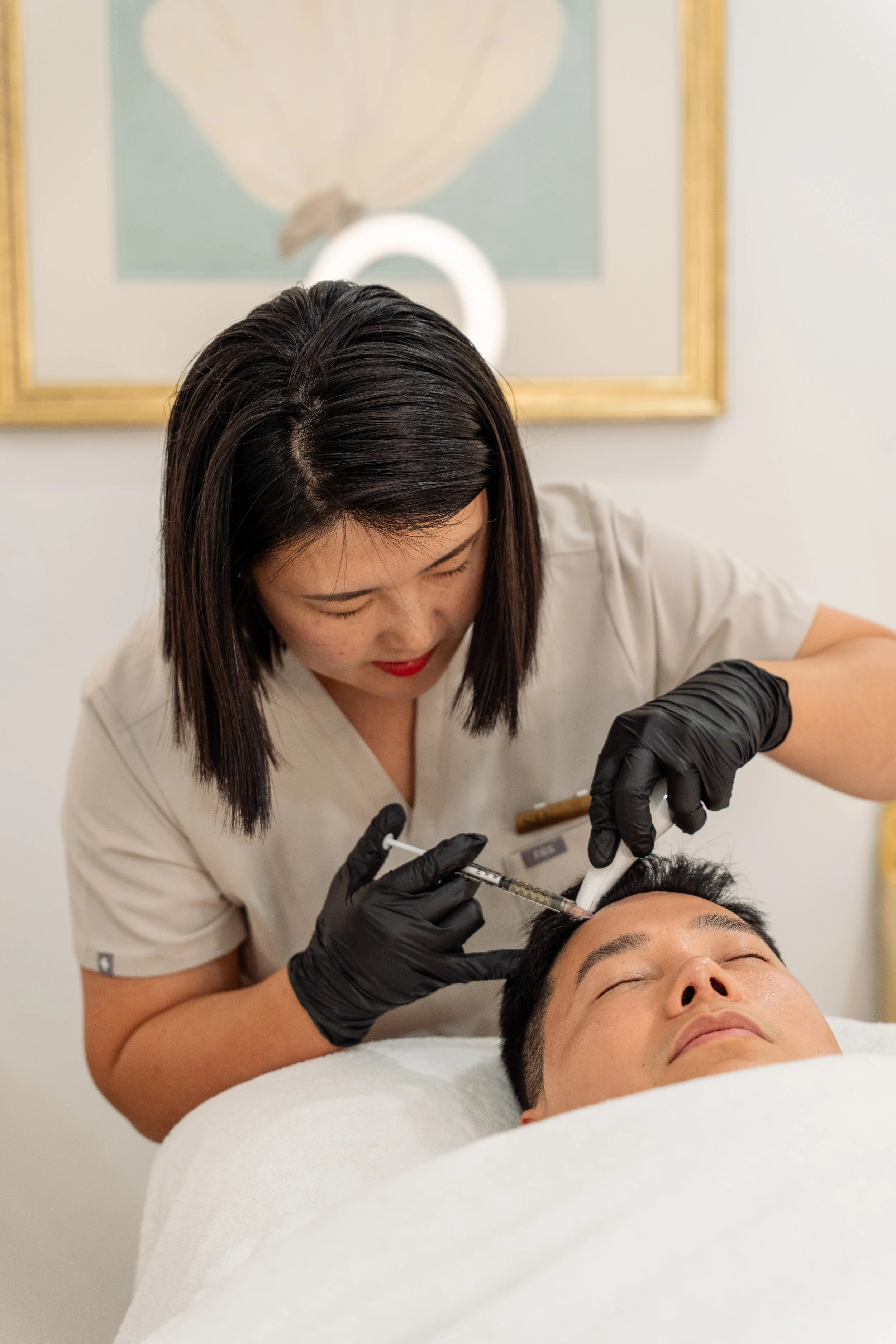 A woman is giving a facial injection to a man lying down with his eyes closed in a spa or medical clinic setting.