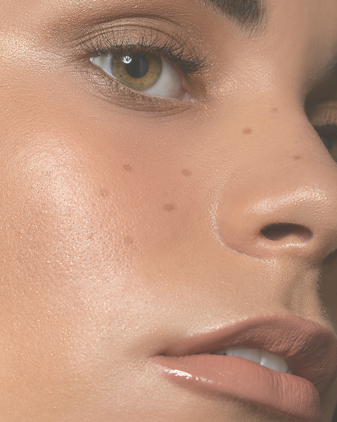 Close-up of a person's face showing a hazel eye, pressed lips, and smooth skin with visible mole and freckles.