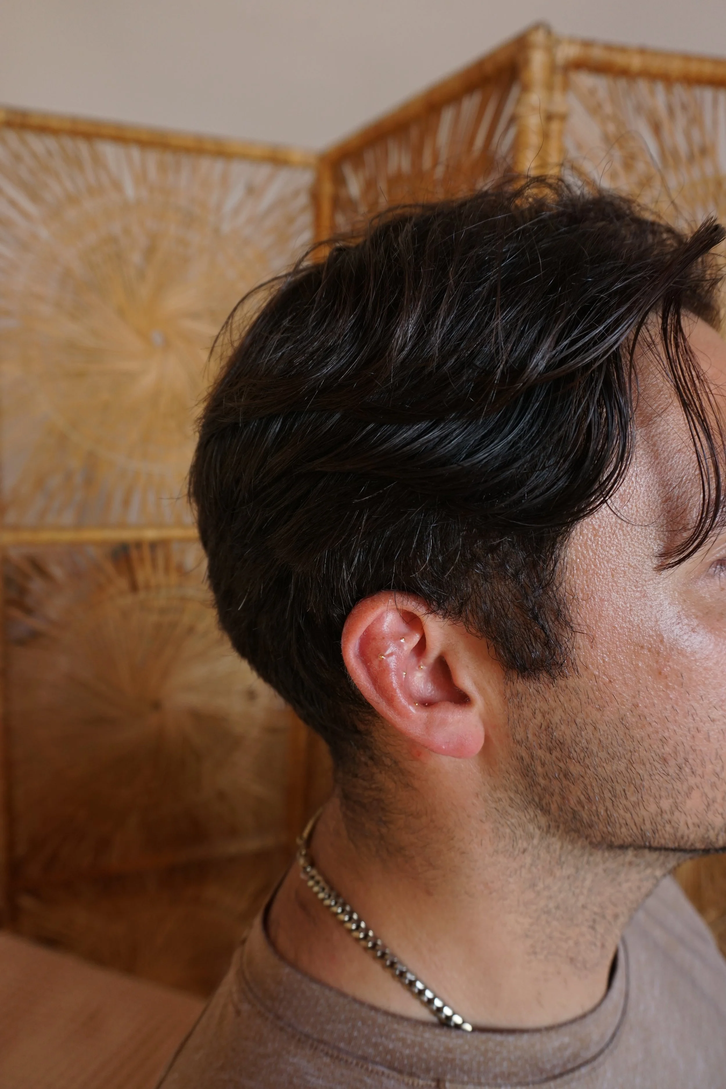 Man seated with ear seeds placed over his ears, whicker design in background.