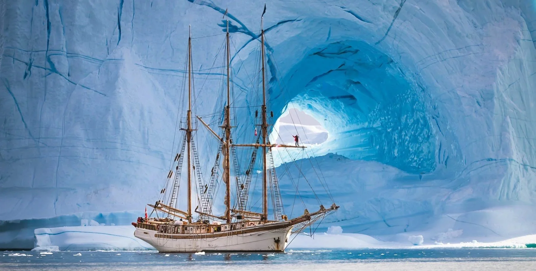 S/V Linden with large ice walls and a blue ice cave in the background.