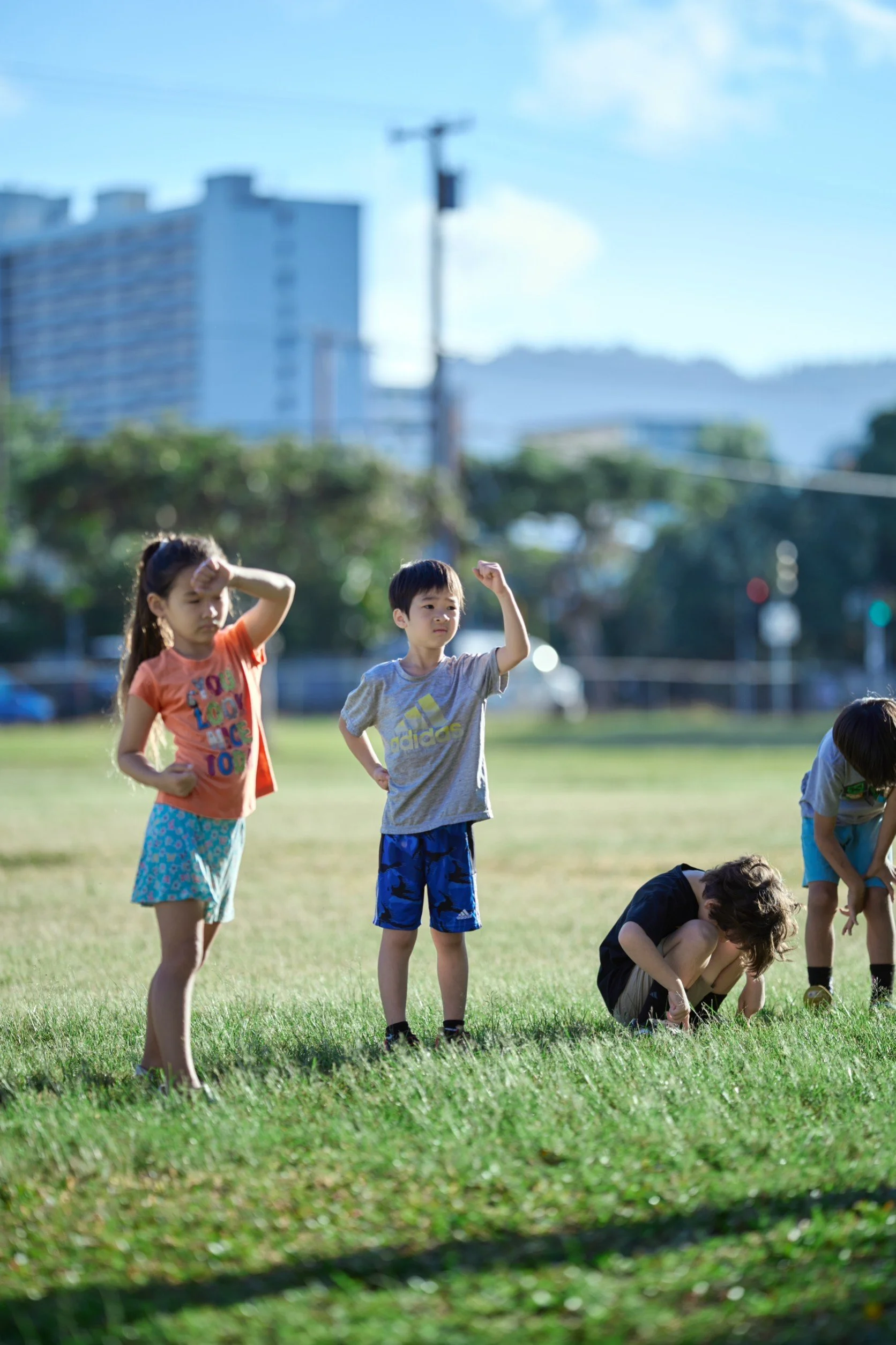Four children playing outdoors on a grassy field on a sunny day.